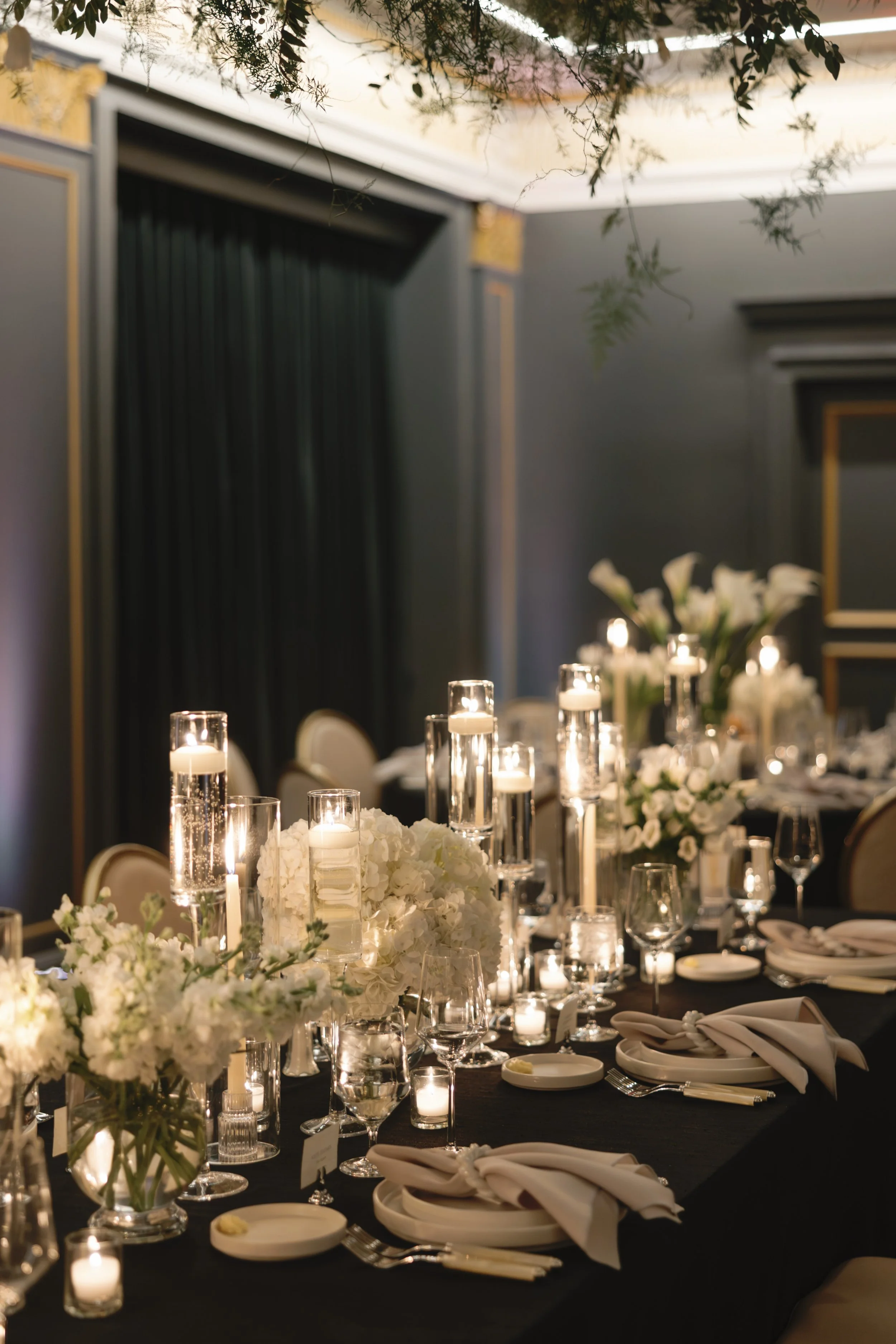 Elegant banquet table decorated with white floral arrangements and votive candles, set for a formal event or wedding reception.