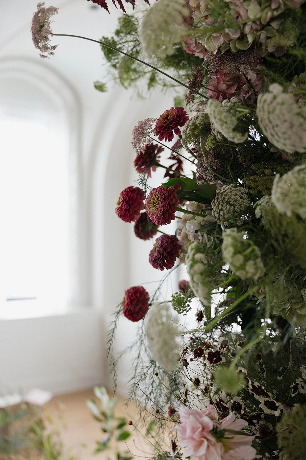 Close-up of a floral arrangement with pink and white flowers, possibly dahlias and hydrangeas, set against a bright, softly lit background.
