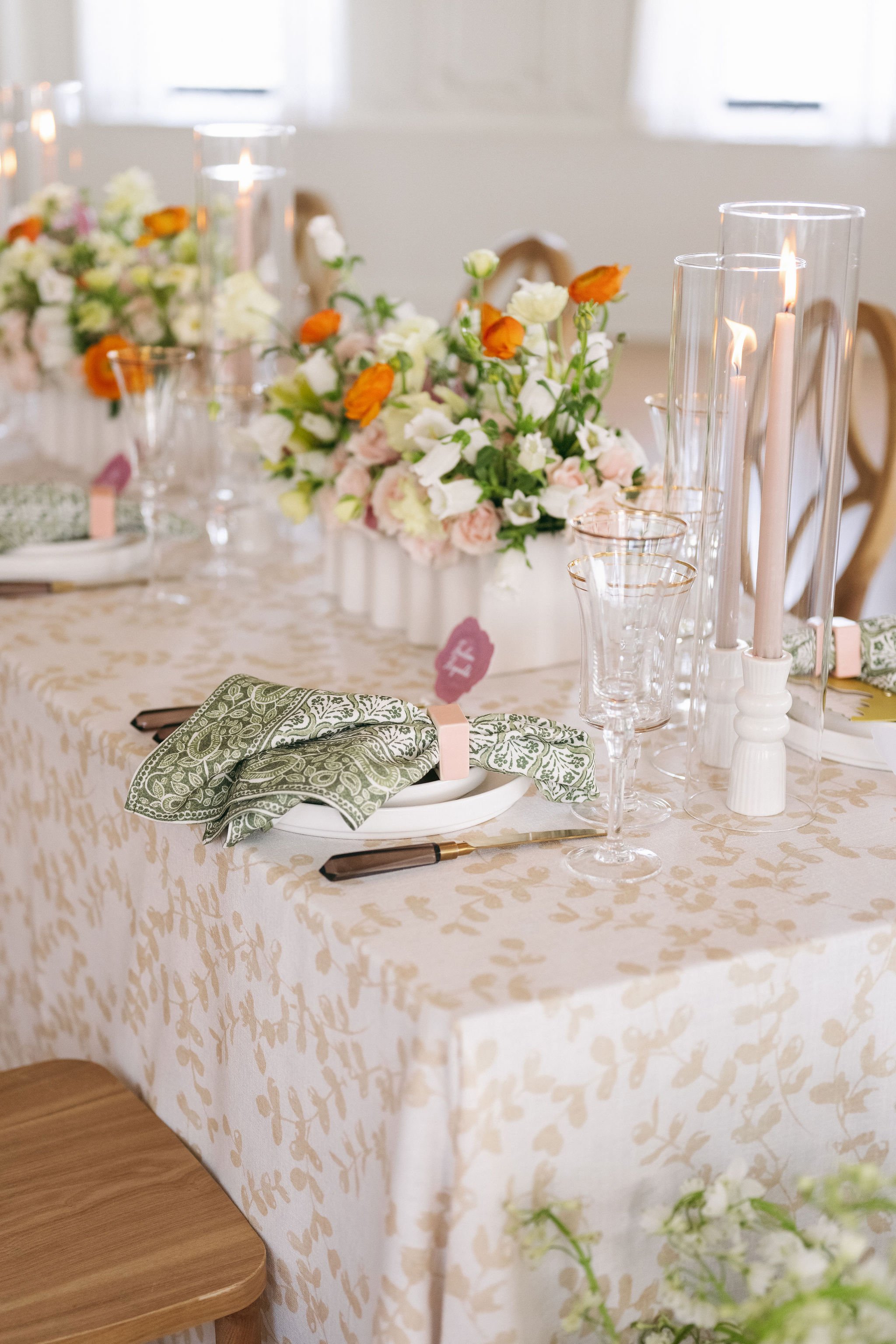 Decorated dining table with floral centerpieces, candles, green patterned napkins, glassware, and place cards.
