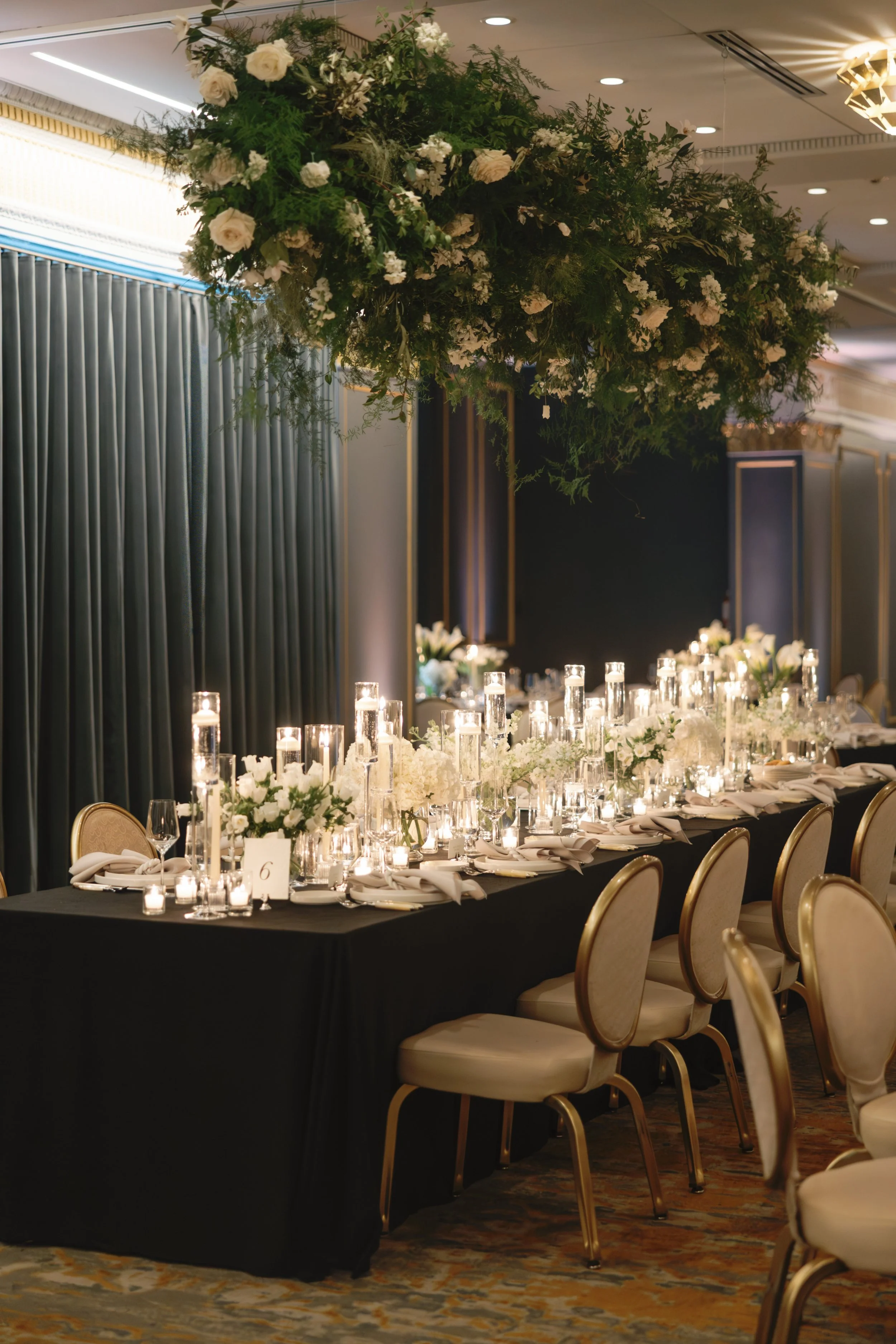 Elegant banquet table decorated with white floral arrangements and numerous lit candles, set in a luxurious event space.