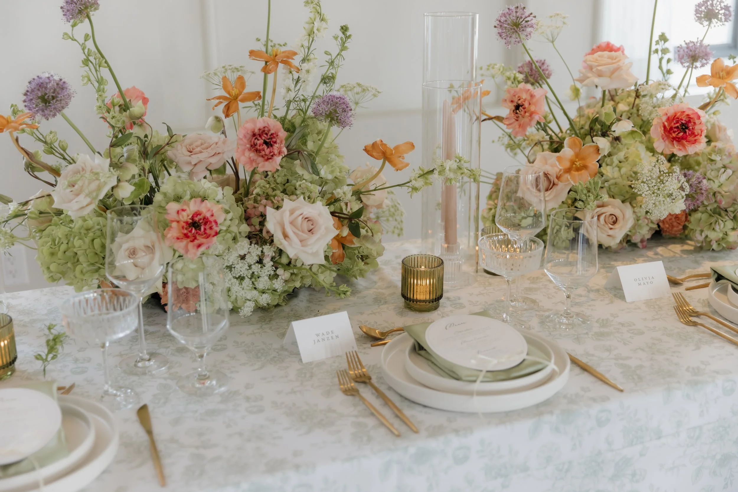 A beautifully decorated banquet table with floral arrangements, candles, wine glasses, and place settings for a formal event.