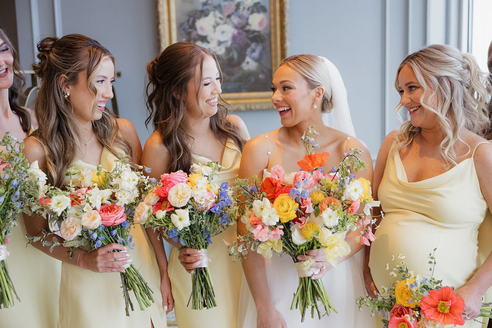 A group of women in yellow dresses holding colorful bouquets, smiling and talking at a wedding celebration.