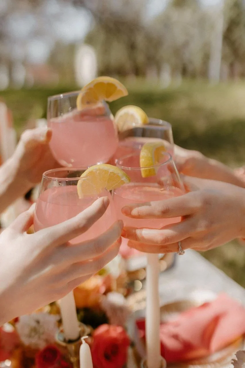 Group of people clinking glasses filled with pink lemonade with lemon slices, outdoors during daytime