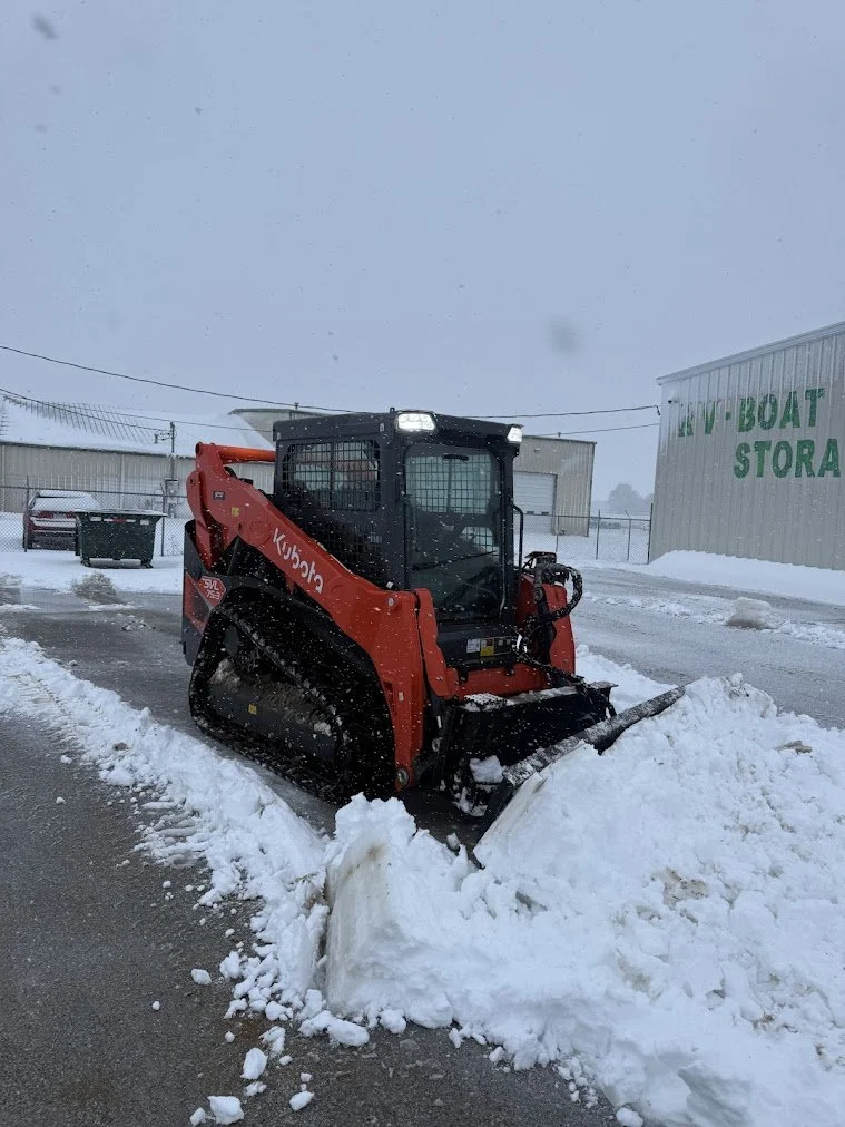 A red Kubota compact skid steer loader clearing snow in a parking lot.