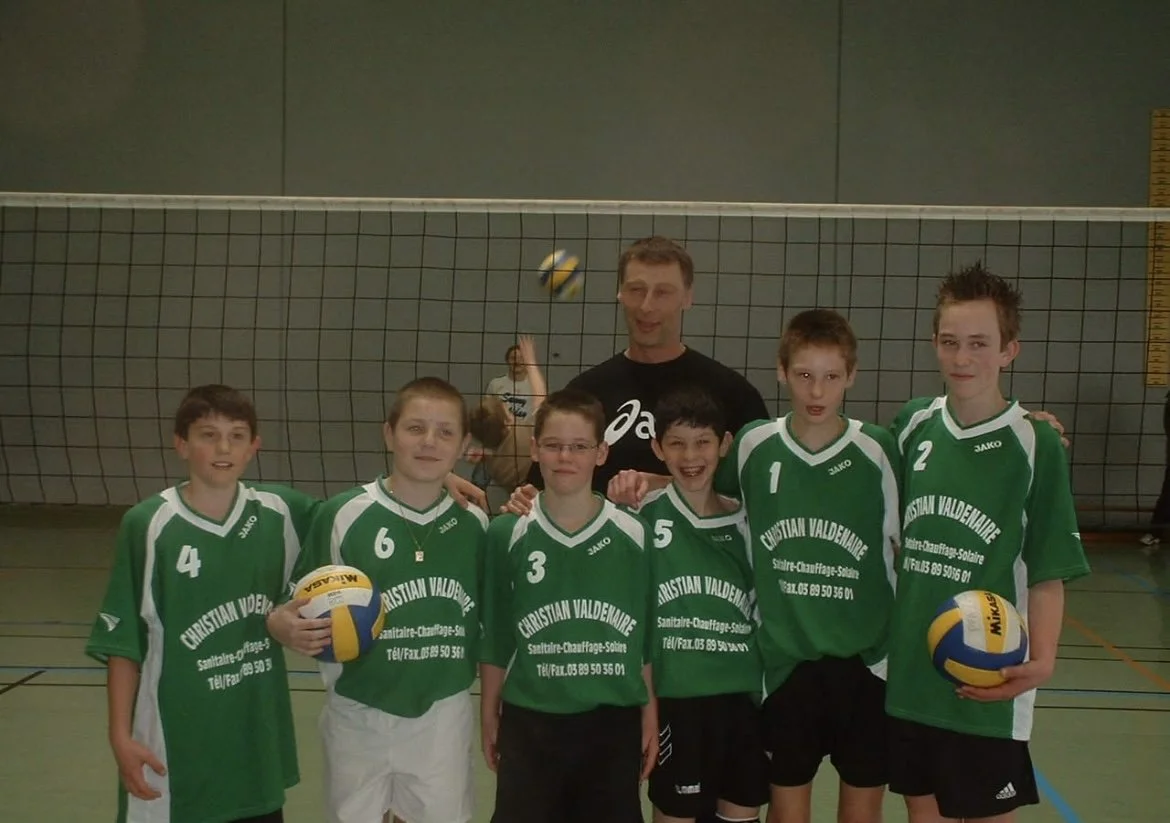 Une équipe de volleyball jeune alsacienne posant pour une photo dans un gymnase avec un entraîneur, tous portant des maillots de volley verts.