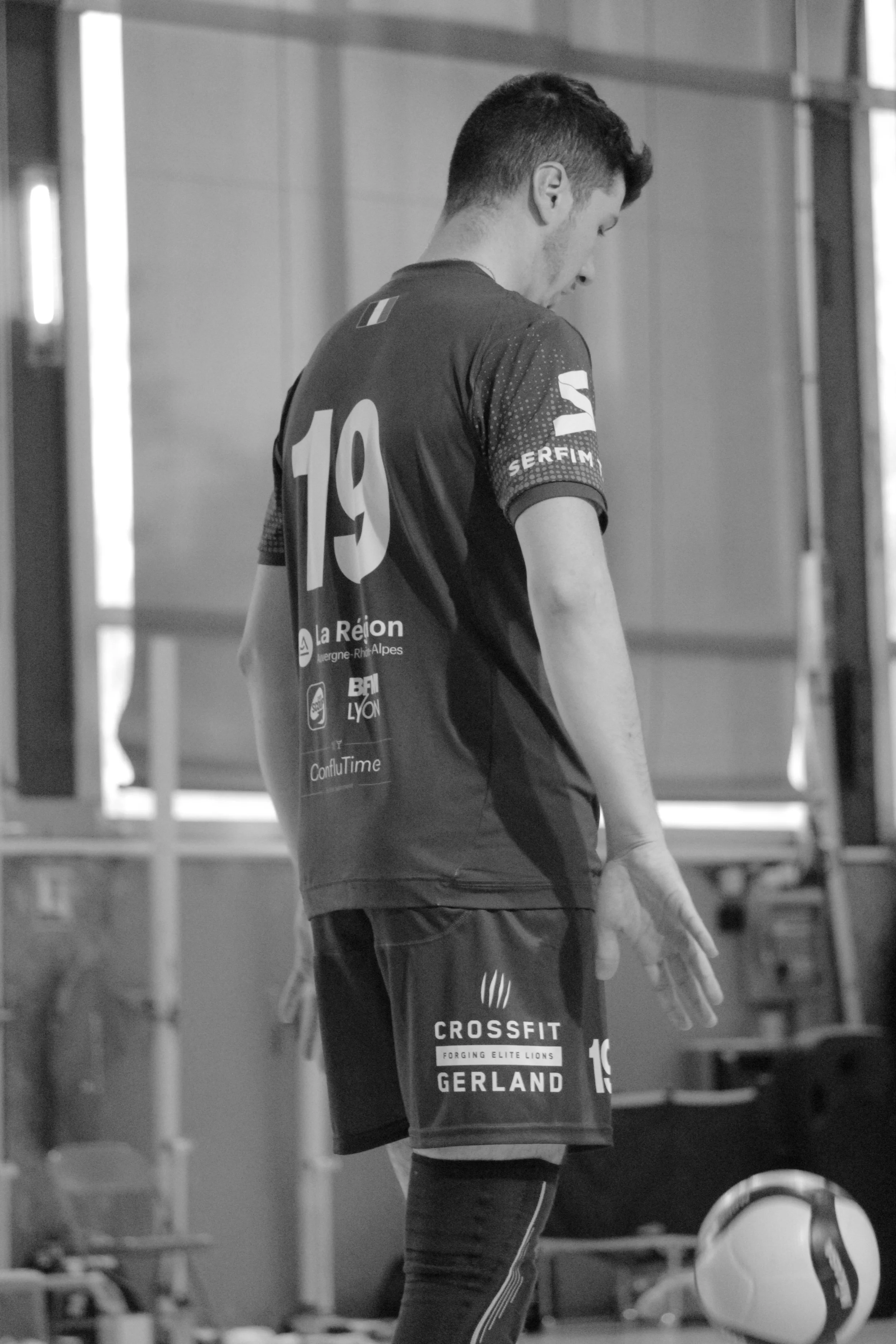 Jeune homme en tenue de sport, portant un maillot de volleyball avec le numéro 19, en pleine concentration mentale dans une salle d'entraînement, avec un ballon de volleyball dans sa main.