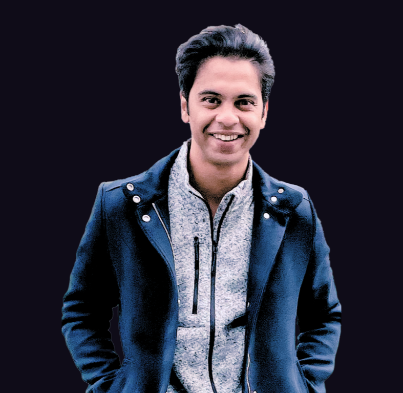 Young man with dark hair smiling, dressed in a gray zip-up sweater and navy jacket, standing against a black background.