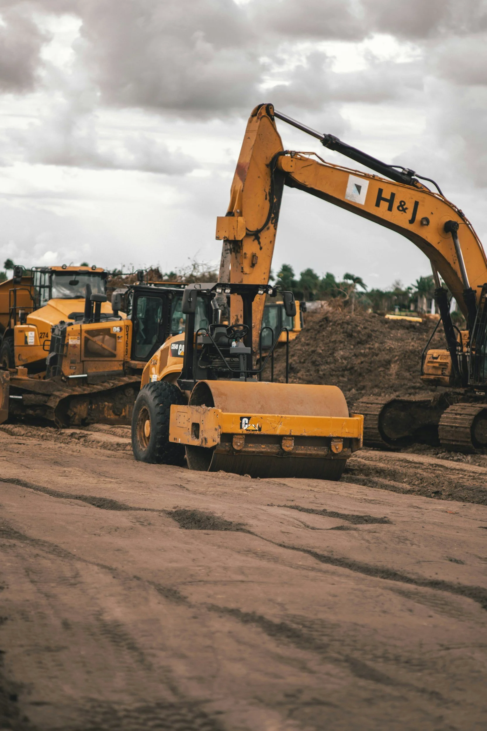 Construction site with yellow heavy machinery, including an excavator and a bulldozer, on a dirt ground under a cloudy sky.