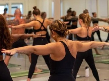 A group of women in a fitness class doing stretching exercises with their arms extended to the sides.