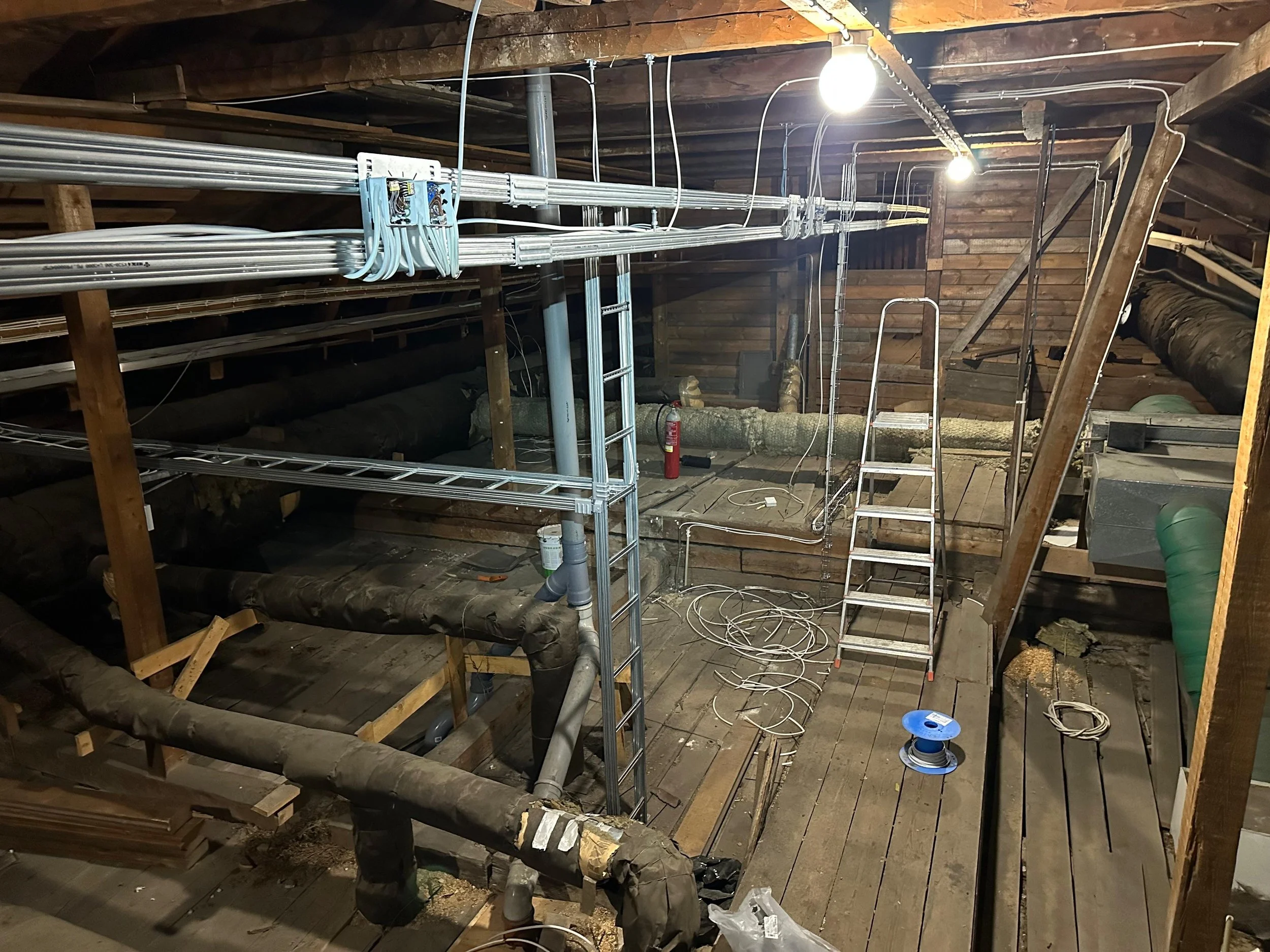 Kohteessa on rakennustyömaa katossa, jossa on putkia, sähköjohtoja ja rakennustelineitä. Vitonen ja katkoviivat, joissa on valaisimia ja työvälineitä.