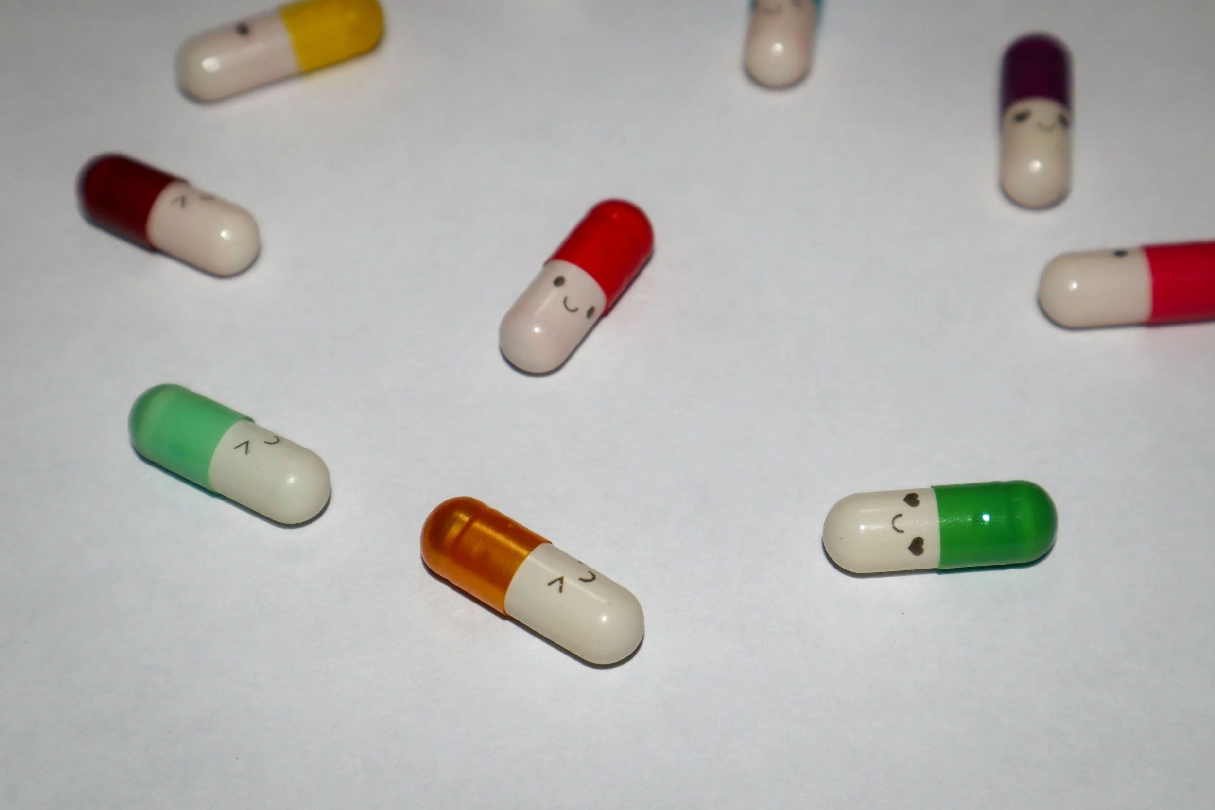 Colorful capsules with smiley face designs scattered on a white surface.