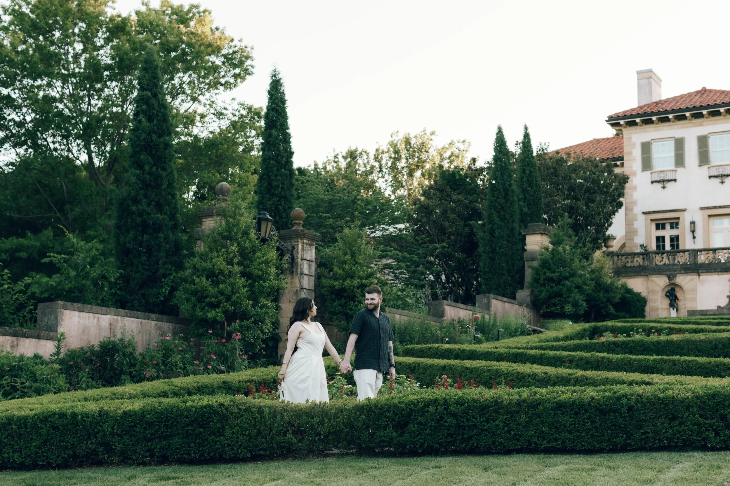 Vast, lush summer gardens at Philbrook Museum Tulsa. Cinematic wedding photography on film featuring a couple walking through an exotic-style landscape with a nostalgic, filmic grain.