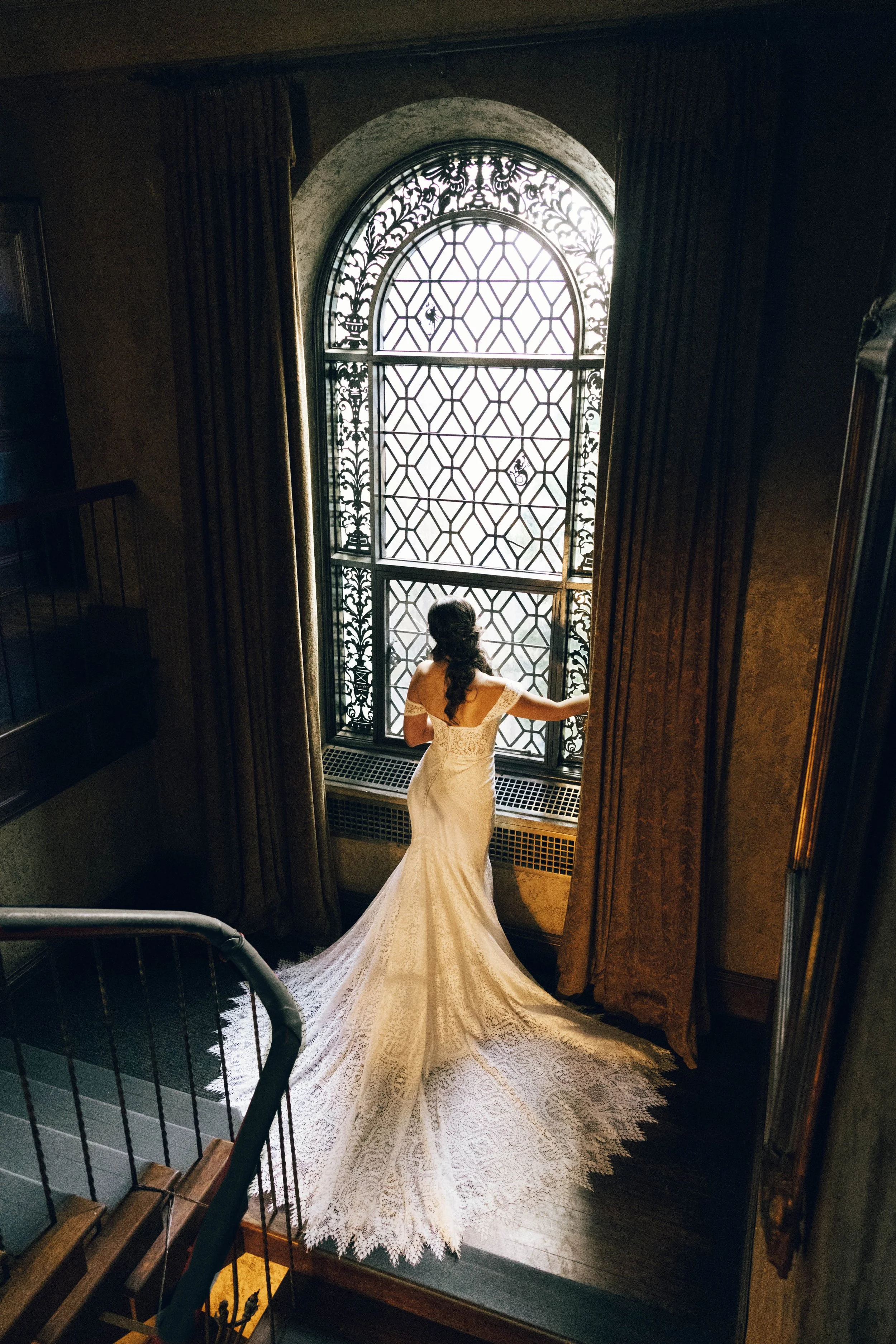 a regal bride portrait at the Dresser Mansion in Tulsa, Oklahoma. The bride stands at a historical window in a dramatic shot captured from behind