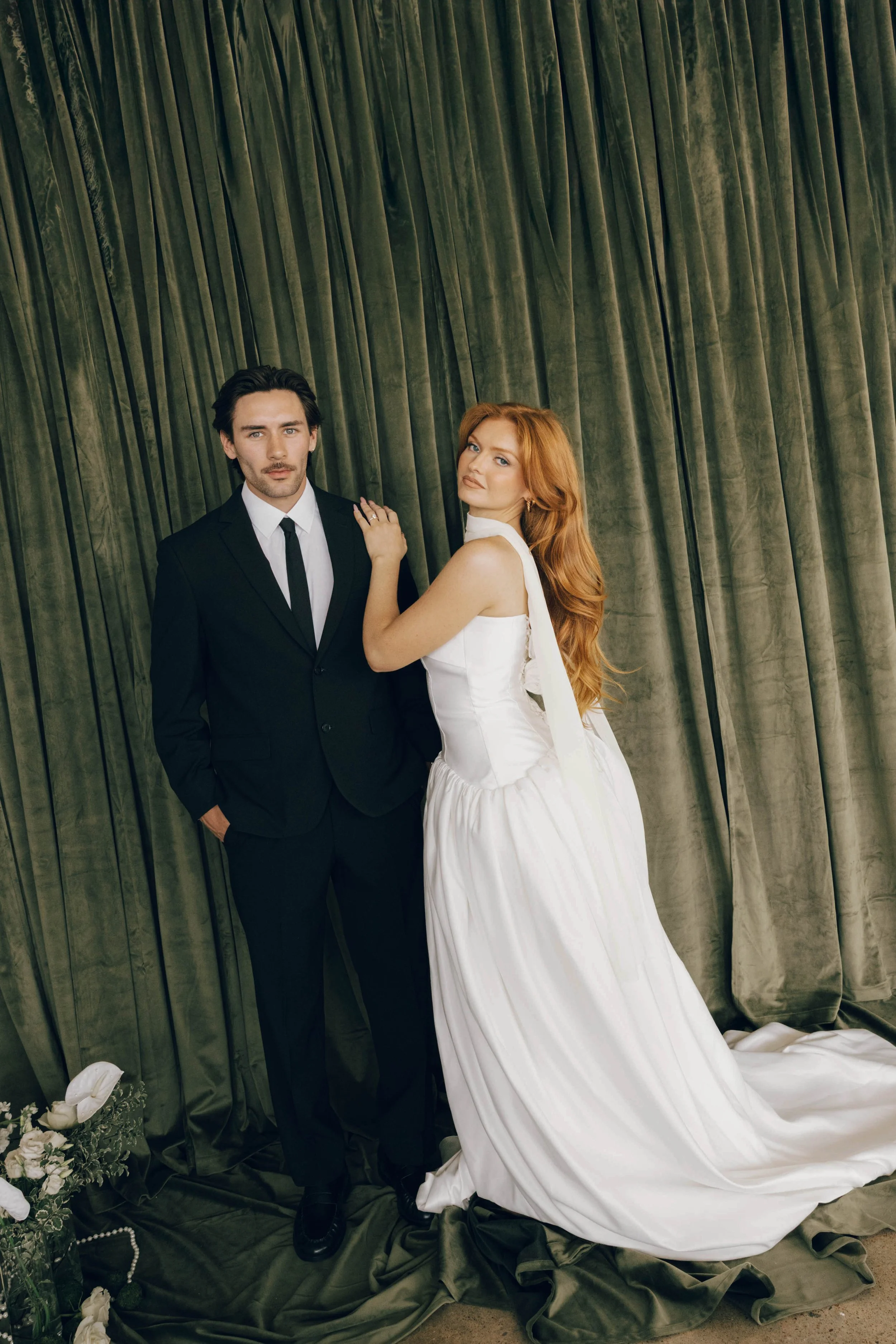 A filmy and cinematic bride and groom portrait against a deep green velvet drapery, featuring a nostalgic, grainy texture.