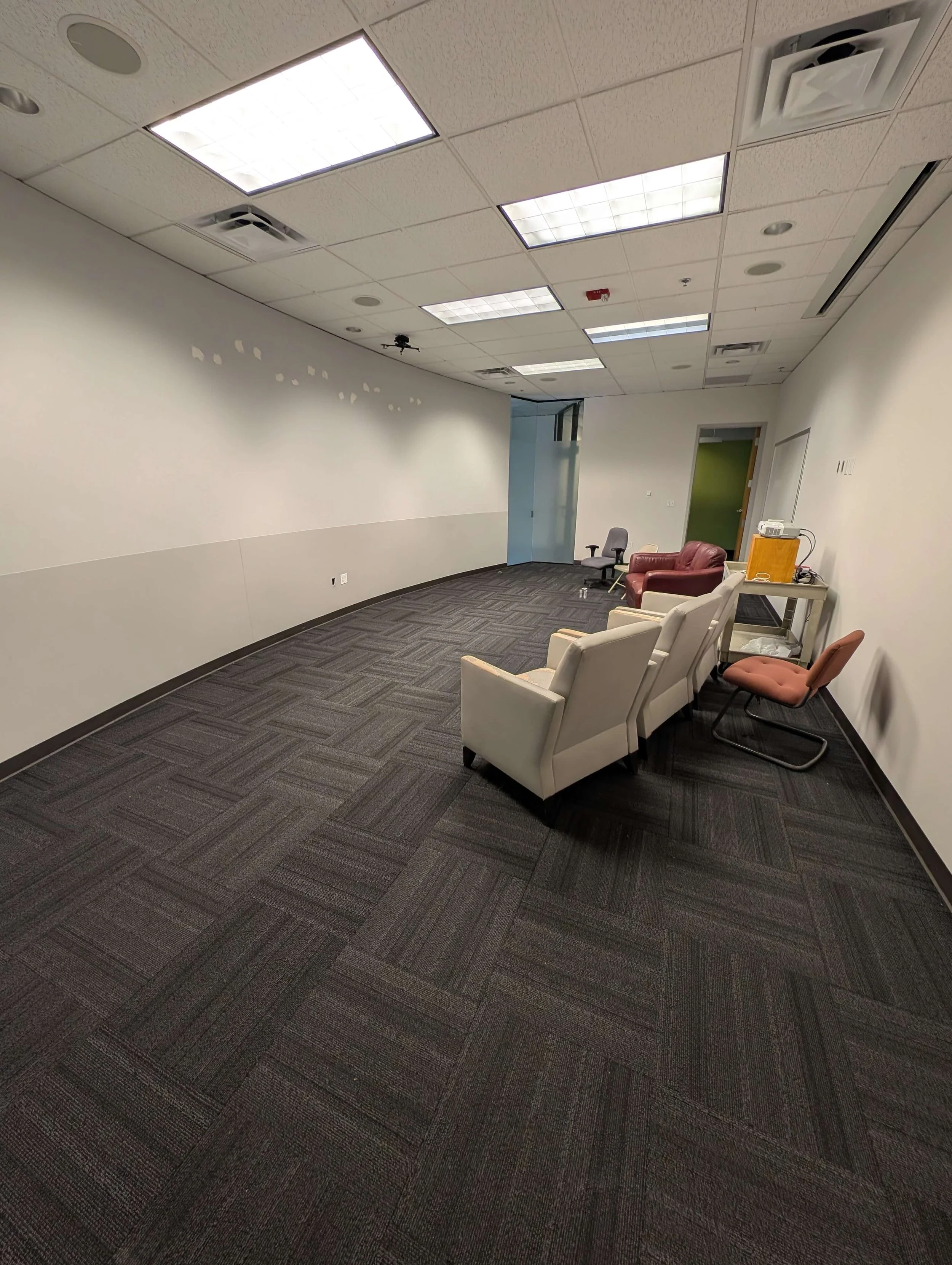 Empty conference room with black carpet, several chairs, sofa, and cart with a projector.