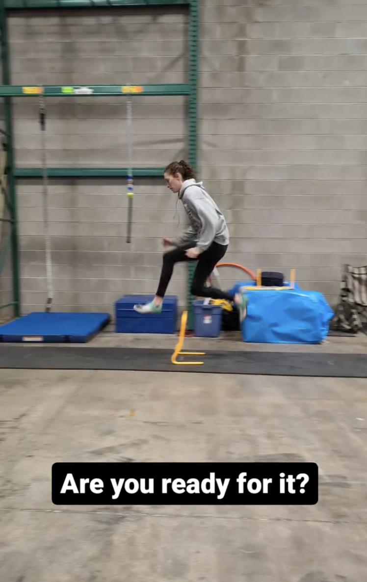 A woman jumping over a small hurdle in an indoor training facility with workout equipment and mats around her, and the caption 'Are you ready for it?' at the bottom.