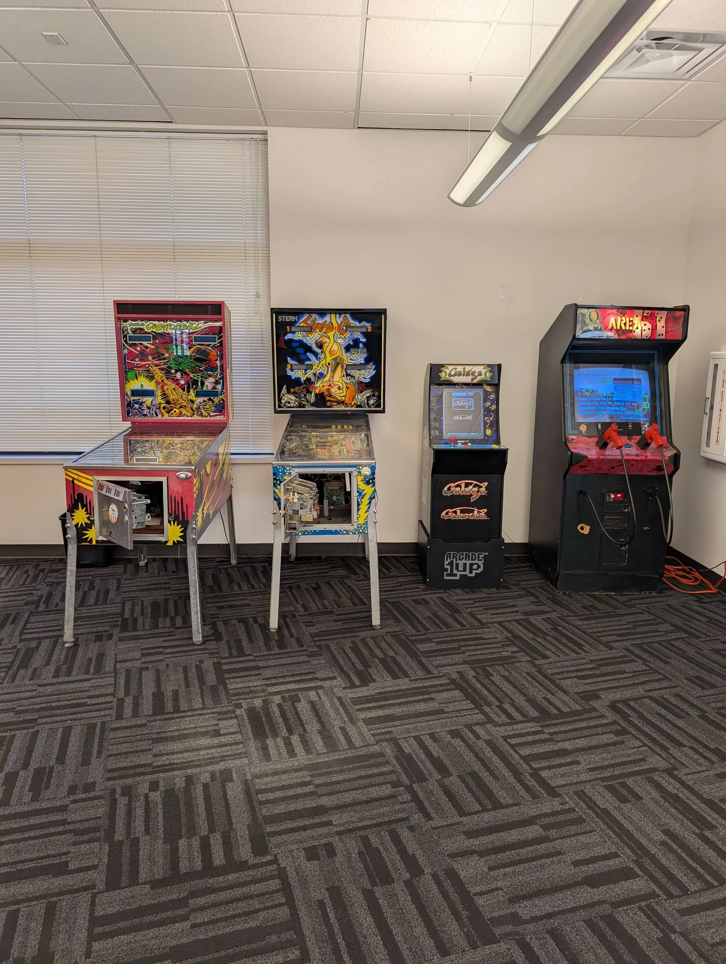 A row of four vintage pinball and arcade machines, with the first two open showing their internal parts, and the last two plugged in and turned on in an indoor game room.