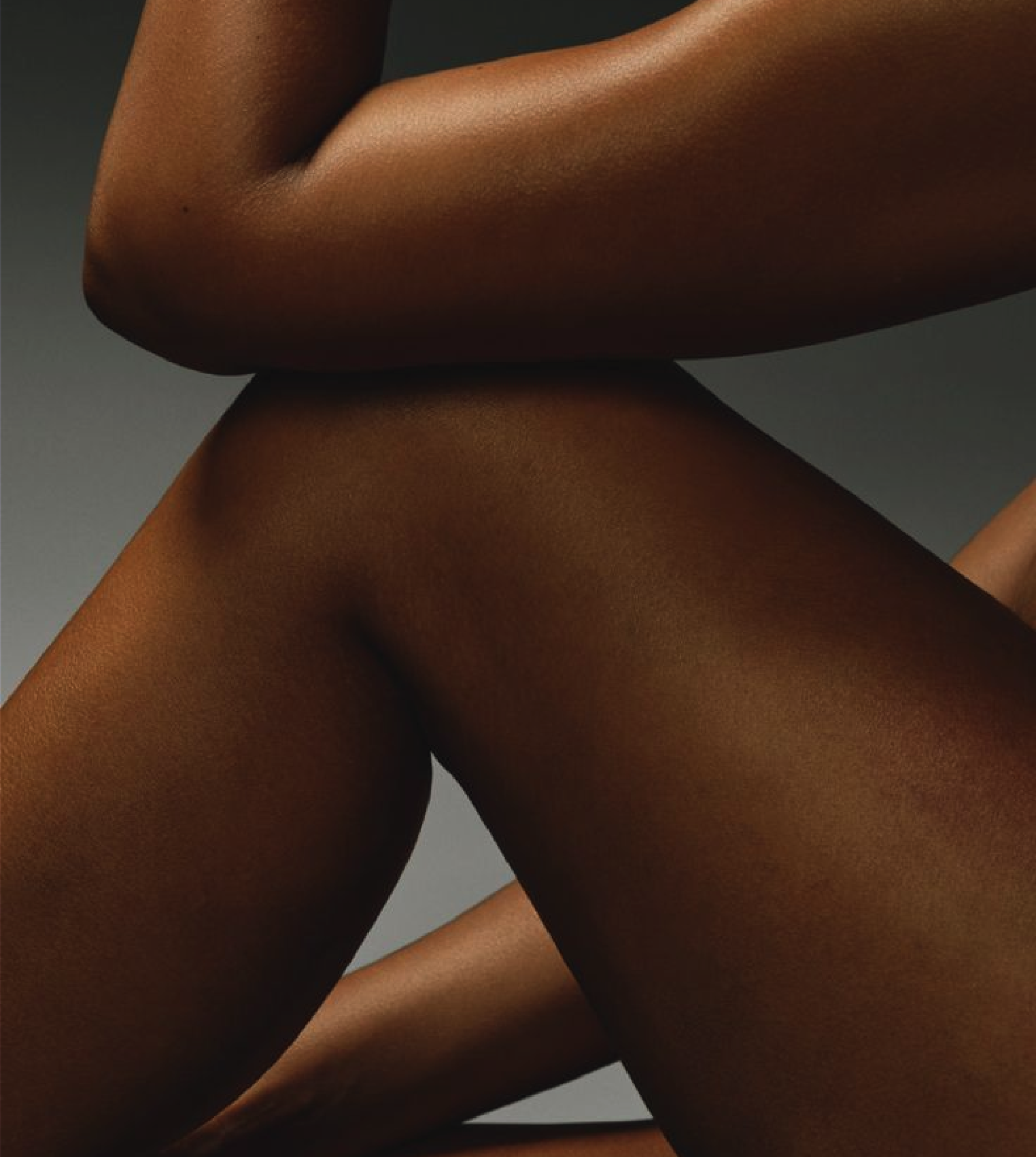 Close-up of a person's crossed arms and legs, showing smooth, dark skin against a gray background.