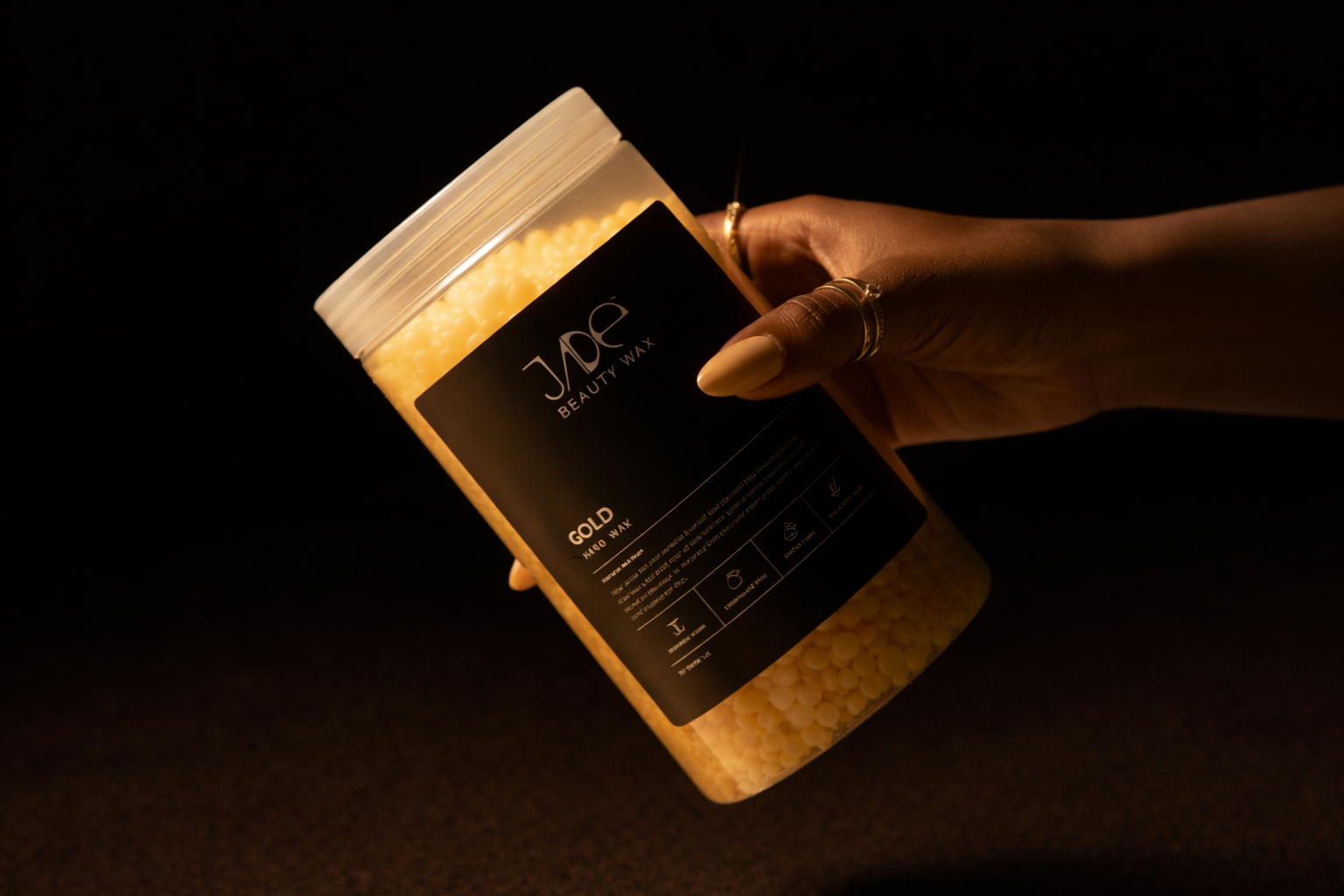 Woman with gold rings and yellow nail polish holding signature wax container