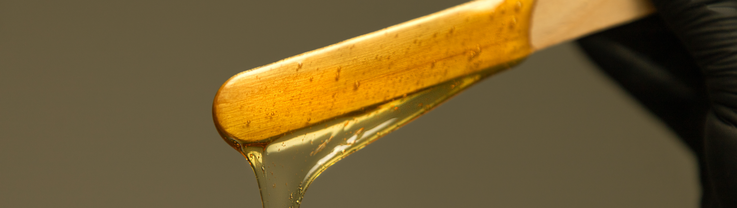 Close-up of a wooden spatula with honey dripping from it.