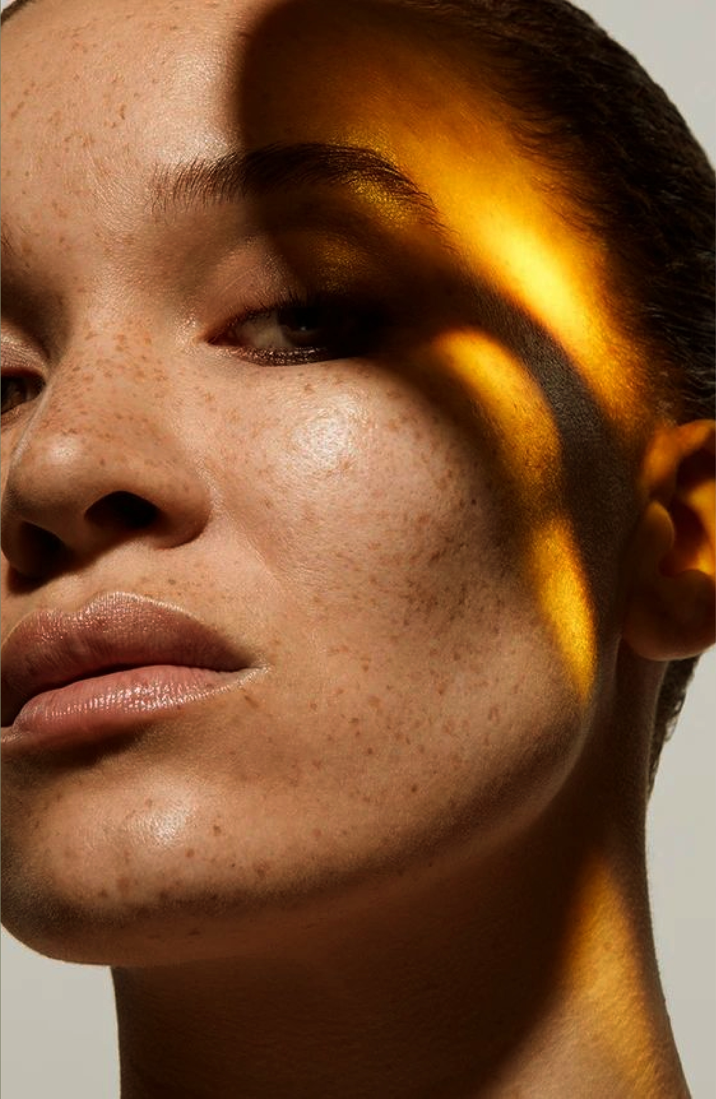 Close-up of a woman's face with natural freckles, lips slightly parted, and a golden light or shadow on the right side of her face.