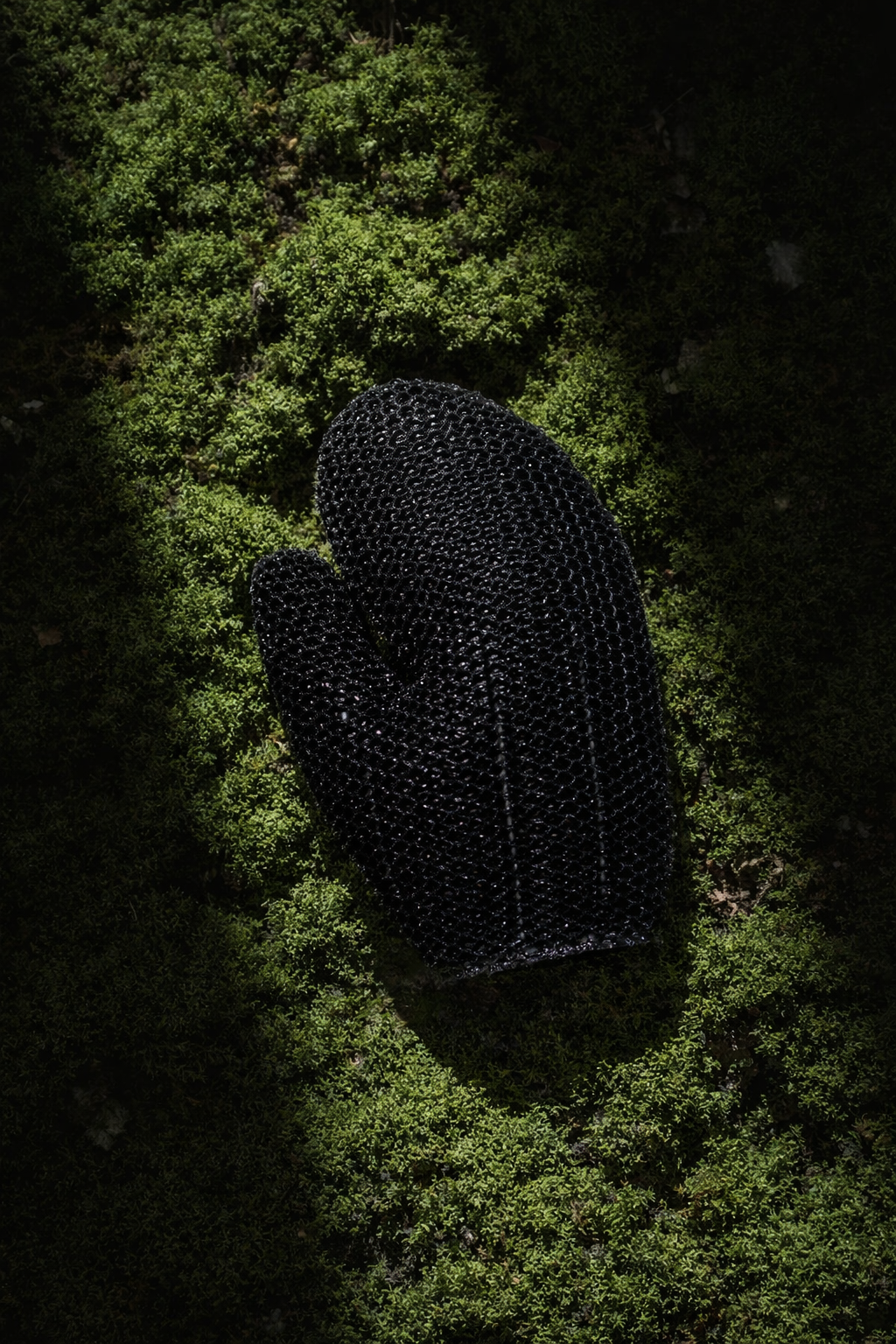A black textured glove resting on green moss ground.