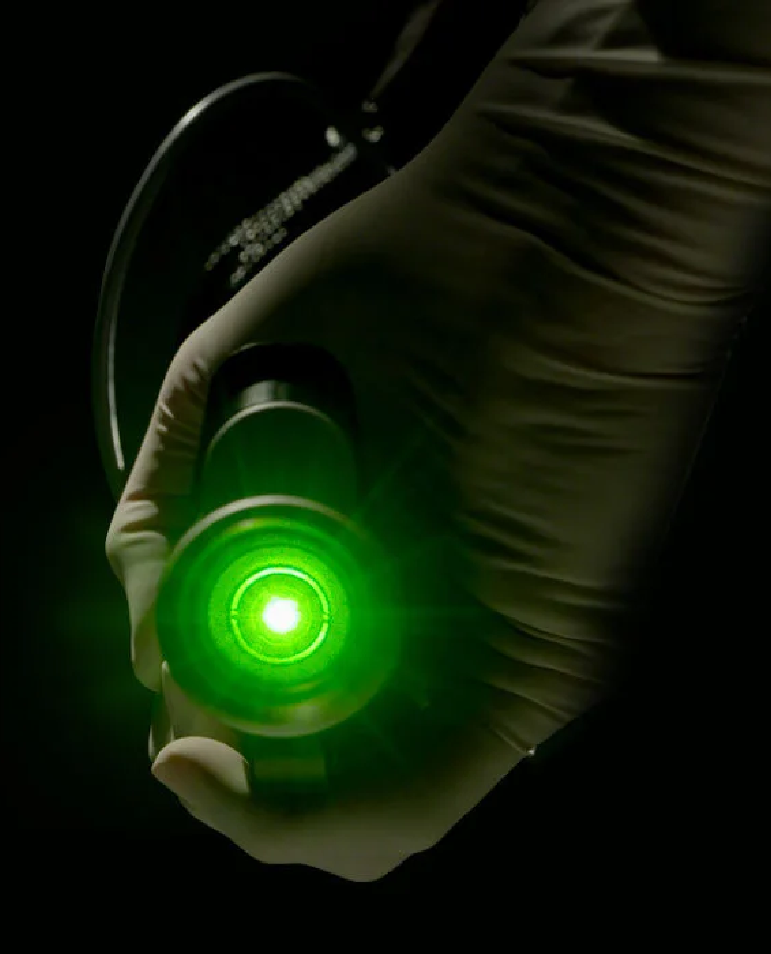 Person holding a black device with a green glowing light, with the hand wearing a white glove.