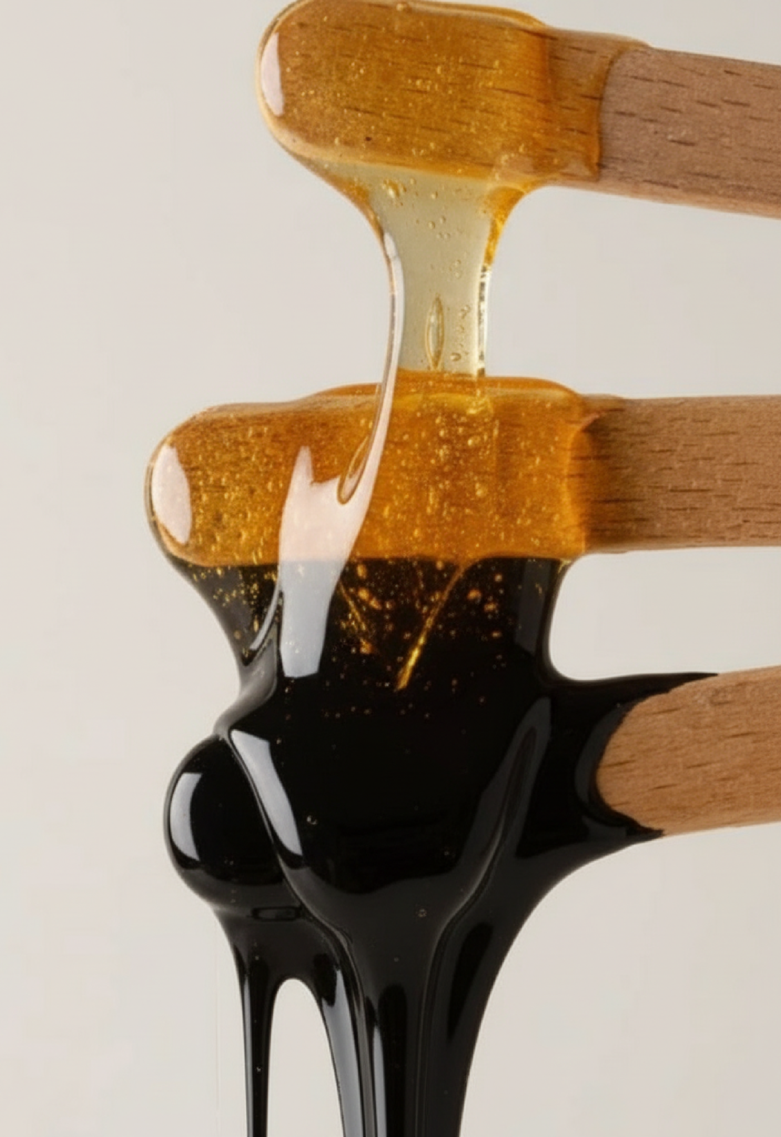 Close-up of three wooden sticks with honey, caramel, and syrup drizzling down.