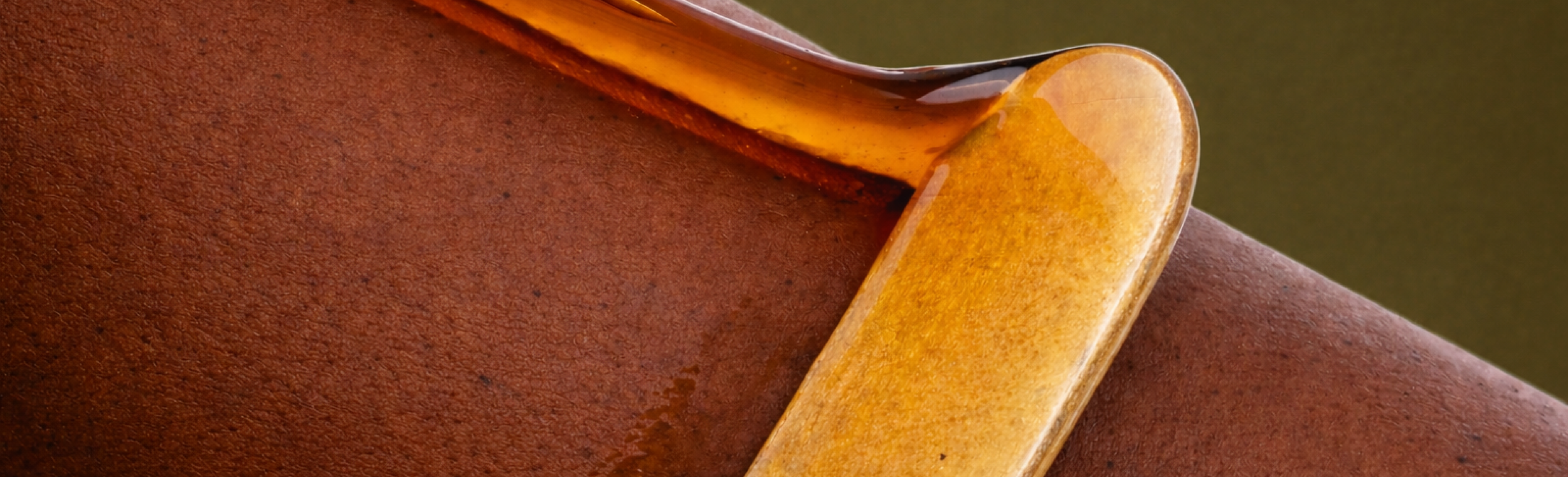Close-up of a ceramic artist's tool, a flat, rounded spatula with a glazed tip, resting on a reddish-brown clay surface.