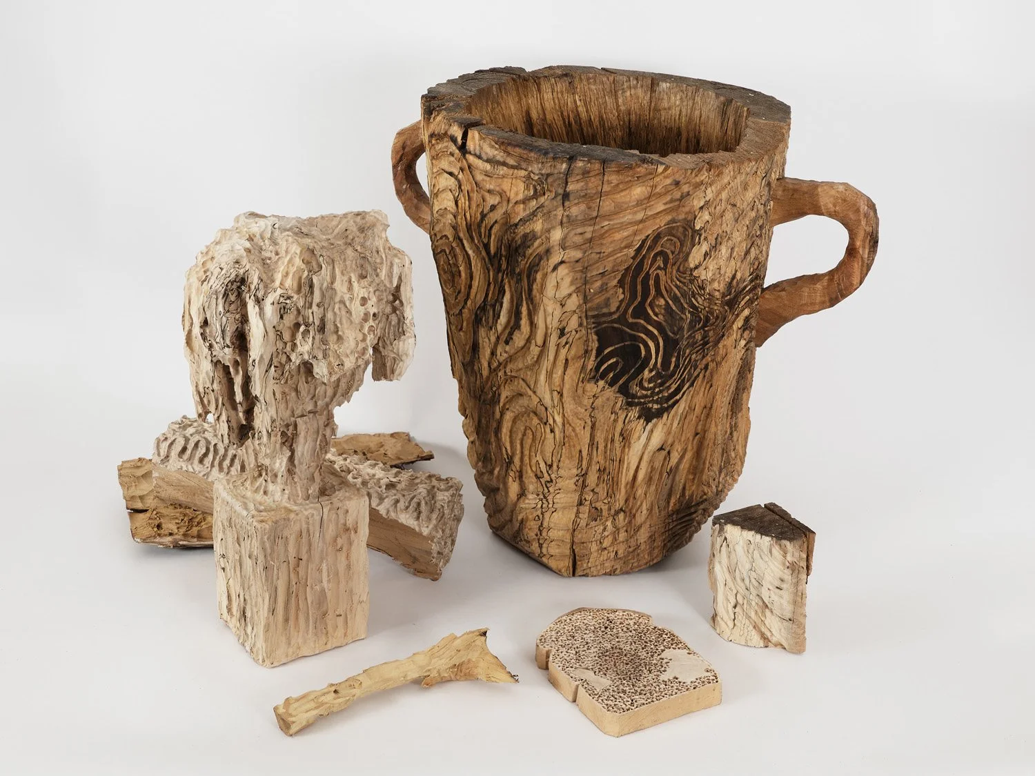 Various carved wooden objects, including a cup with handles and a decorative piece, on a white background.