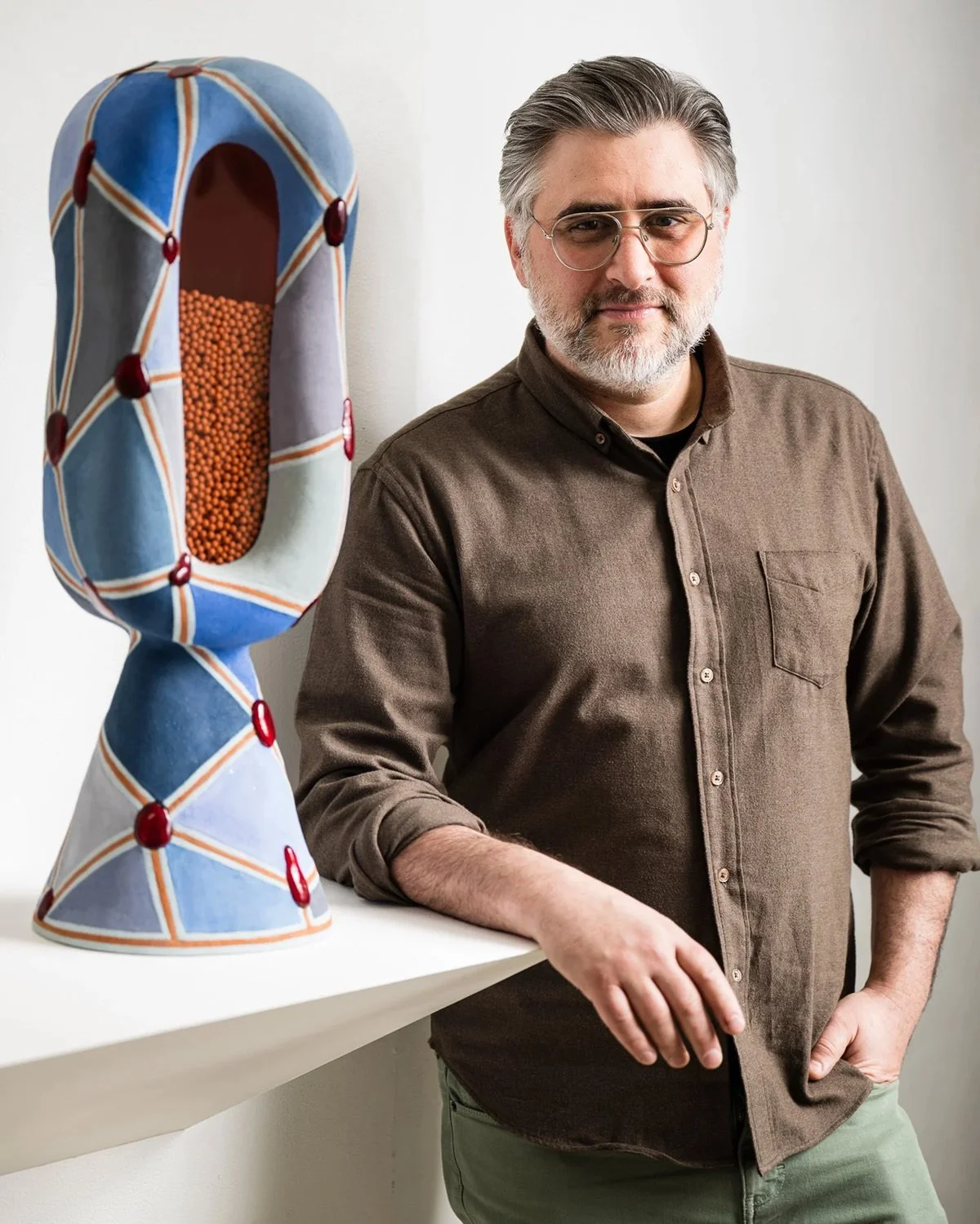 A photo of artist and photographer, Saul Chernick standing next to one of his abstract sculptures in gallery setting.