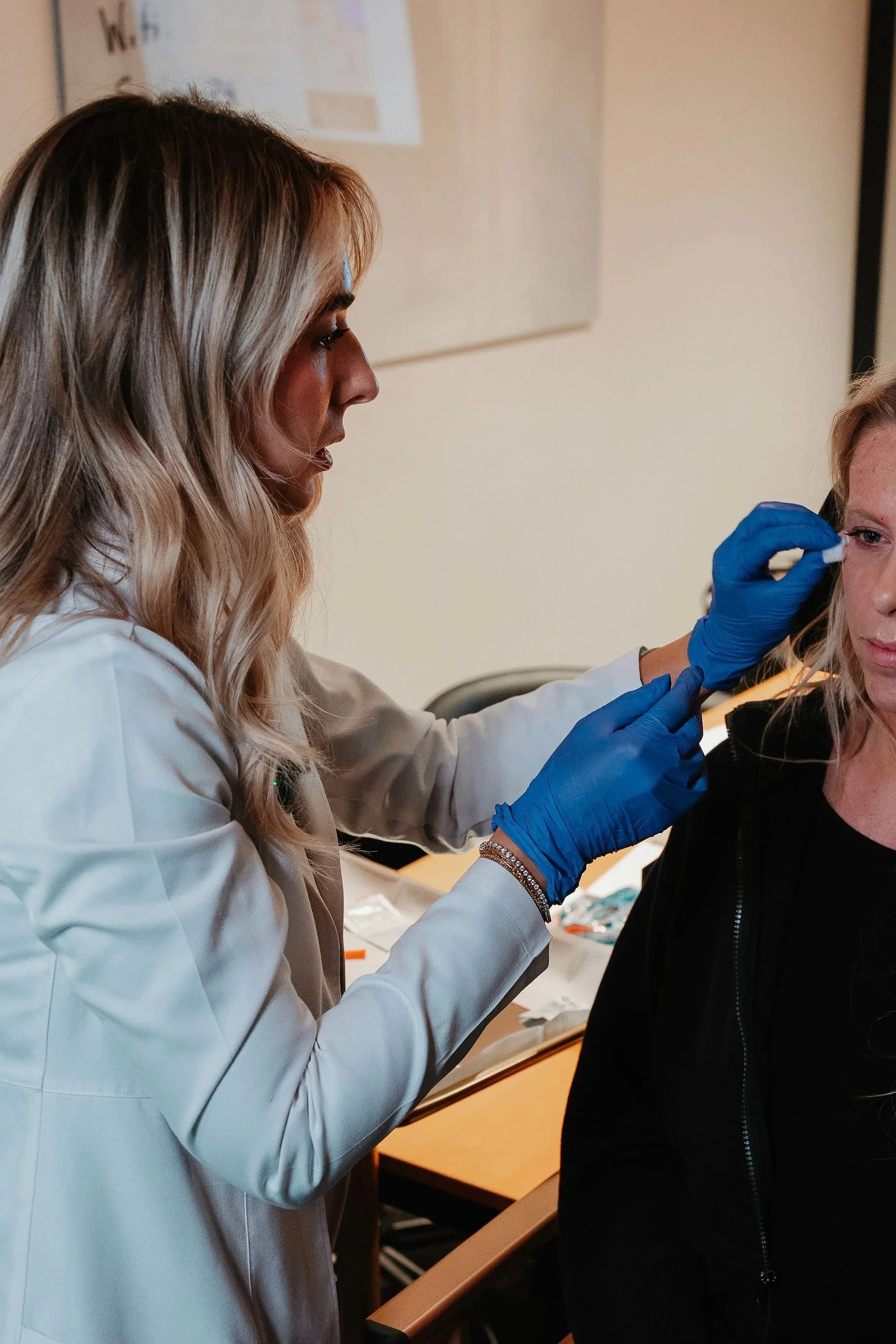 A healthcare professional wearing blue gloves is administering a facial injection to a woman with blonde hair.