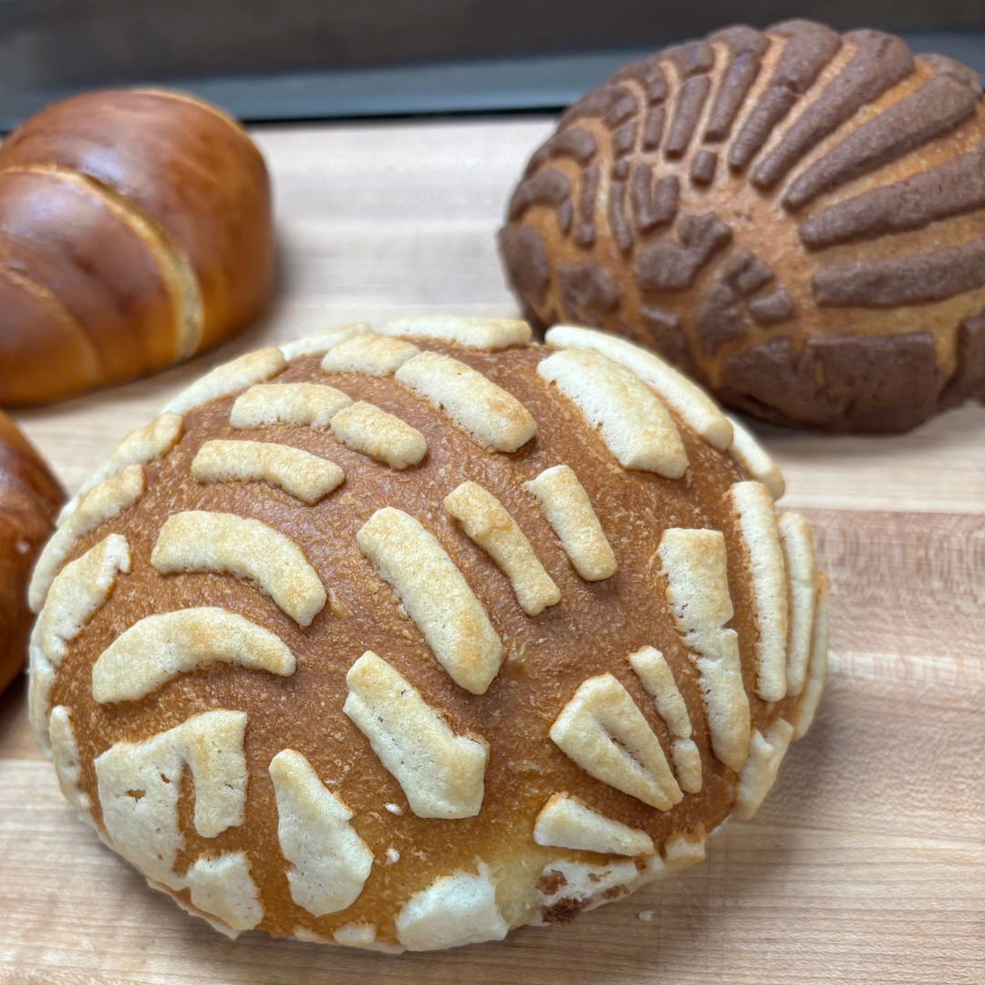 Close-up of assorted baked goods on a wooden surface, including a bread roll with icing, chocolate and vanilla bread, and a pastry with white icing and striped pattern.