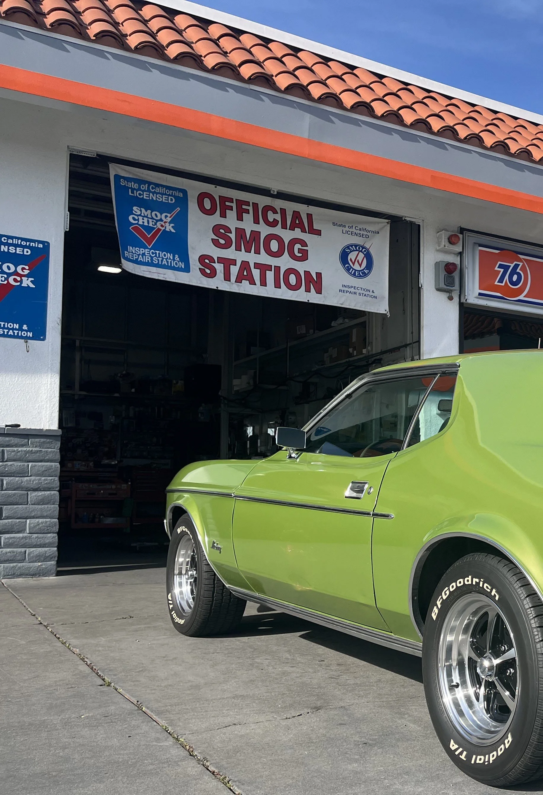 A bright green vintage car parked outside a garage with a sign that reads 'Official Smog Station'.