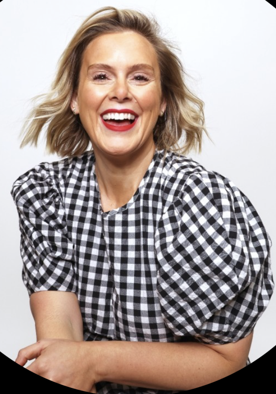 Happy woman with blonde hair in a checkered black and white shirt smiling against a plain background.