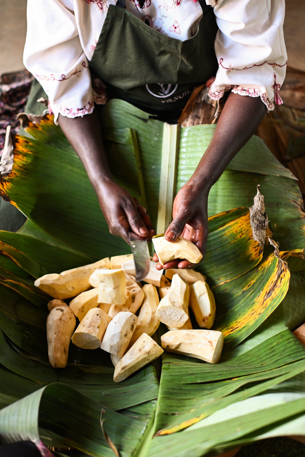 Person schneidet Yamswurzel auf einem großen grünen Bananenblatt