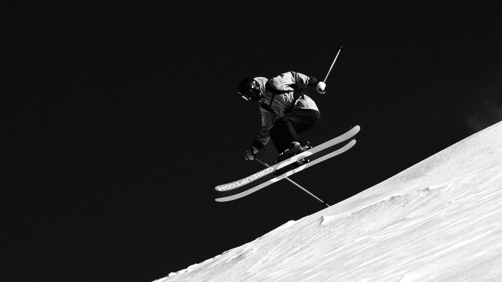 Skieur en plein saut dans la montagne enneigée, vue en contre-plongée, ciel noir en arrière-plan.