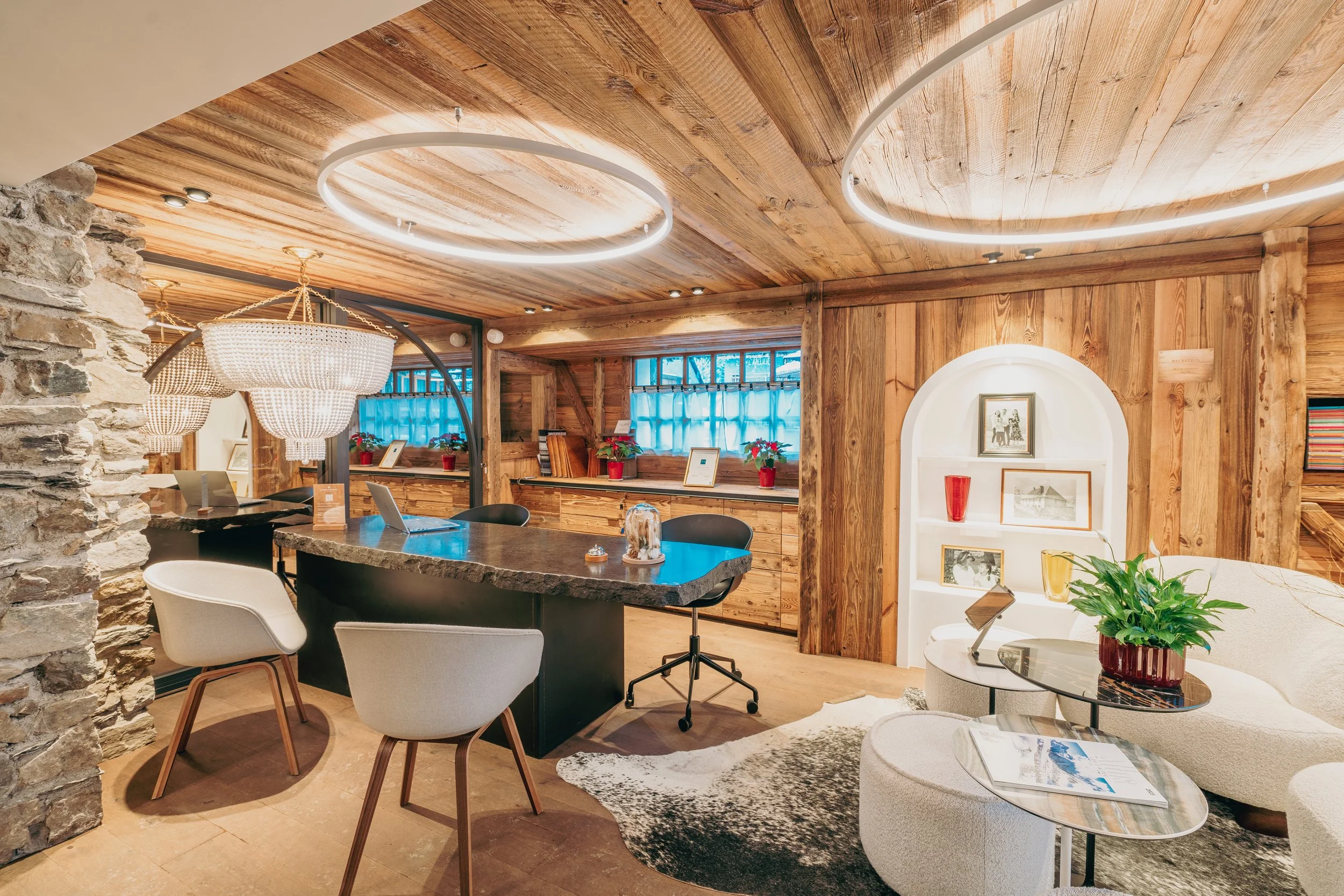 Un intérieur chaleureux avec murs et plafond en bois, un comptoir en pierre, et un mobilier moderne dont un canapé blanc, une table basse en verre, des chaises confortables, et des objets décoratifs, dans un style cosy et contemporain.