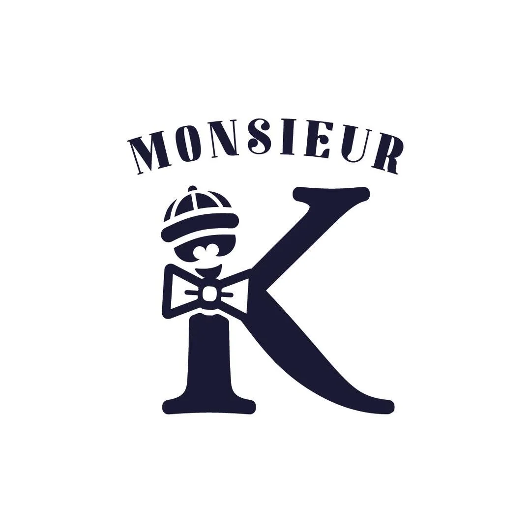 Logo noir avec le mot 'Monsieur' au-dessus d'un grand 'K' stylisé. Le 'K' a un visage souriant, porte un chapeau, une paire de lunettes et un nœud papillon.