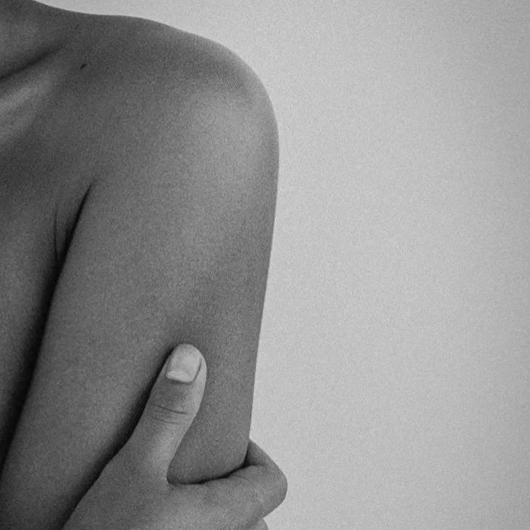Close-up of a person’s arm and shoulder, with their hand resting on their upper arm, in black and white.