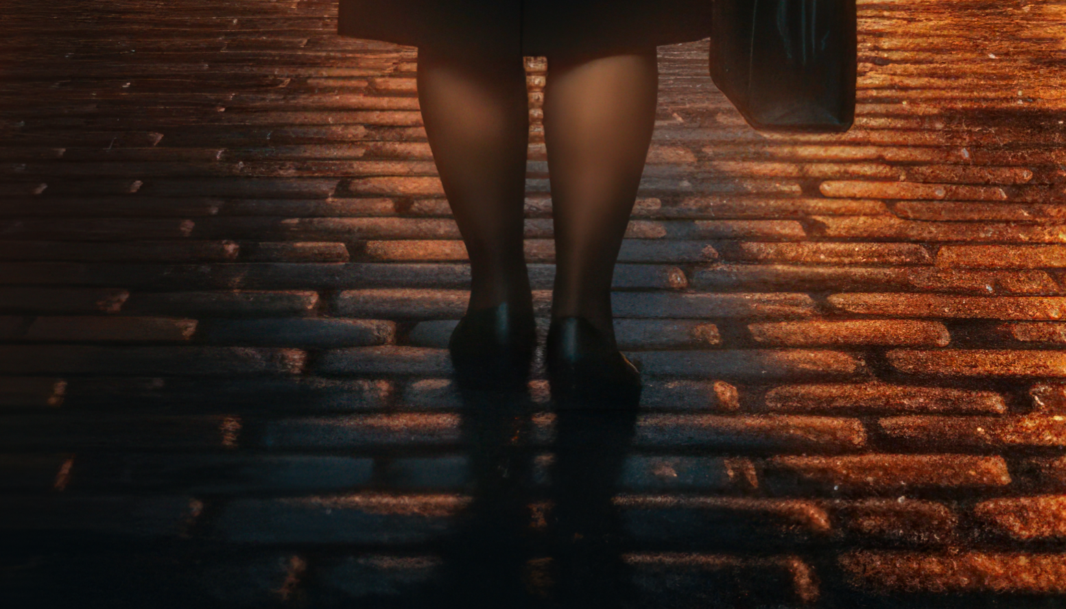 Close-up of a person's legs and feet wearing black shoes and black stockings, walking on a cobblestone street at dusk, with a bag hanging from one arm.