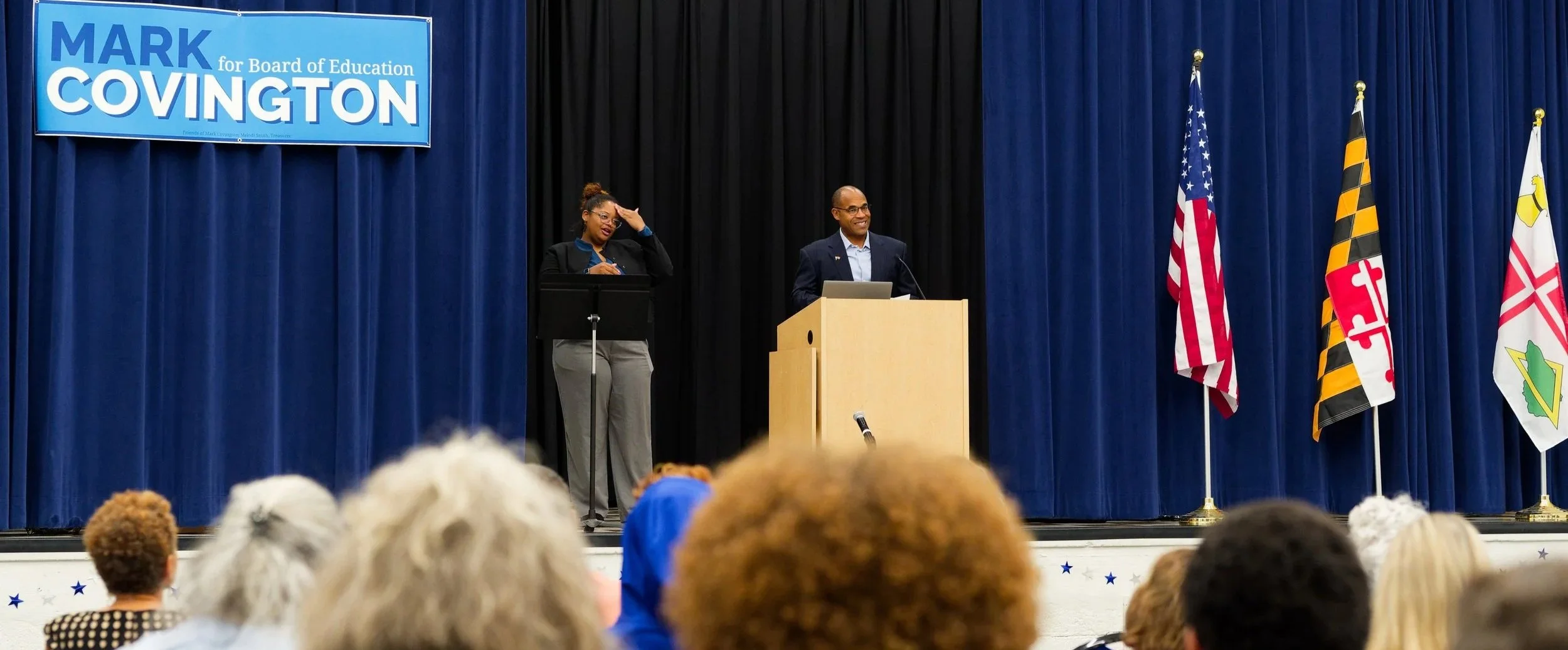 Mark Covington and an ASL interpreter standing on a stage at the Harriet Tubman Cultural Center in Howard County speaking to a crowd