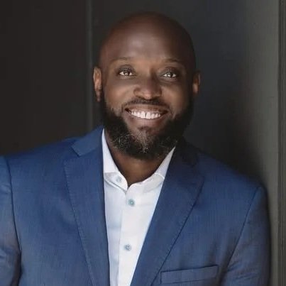 Portrait of a man with a beard in a blue suit and white shirt, smiling.