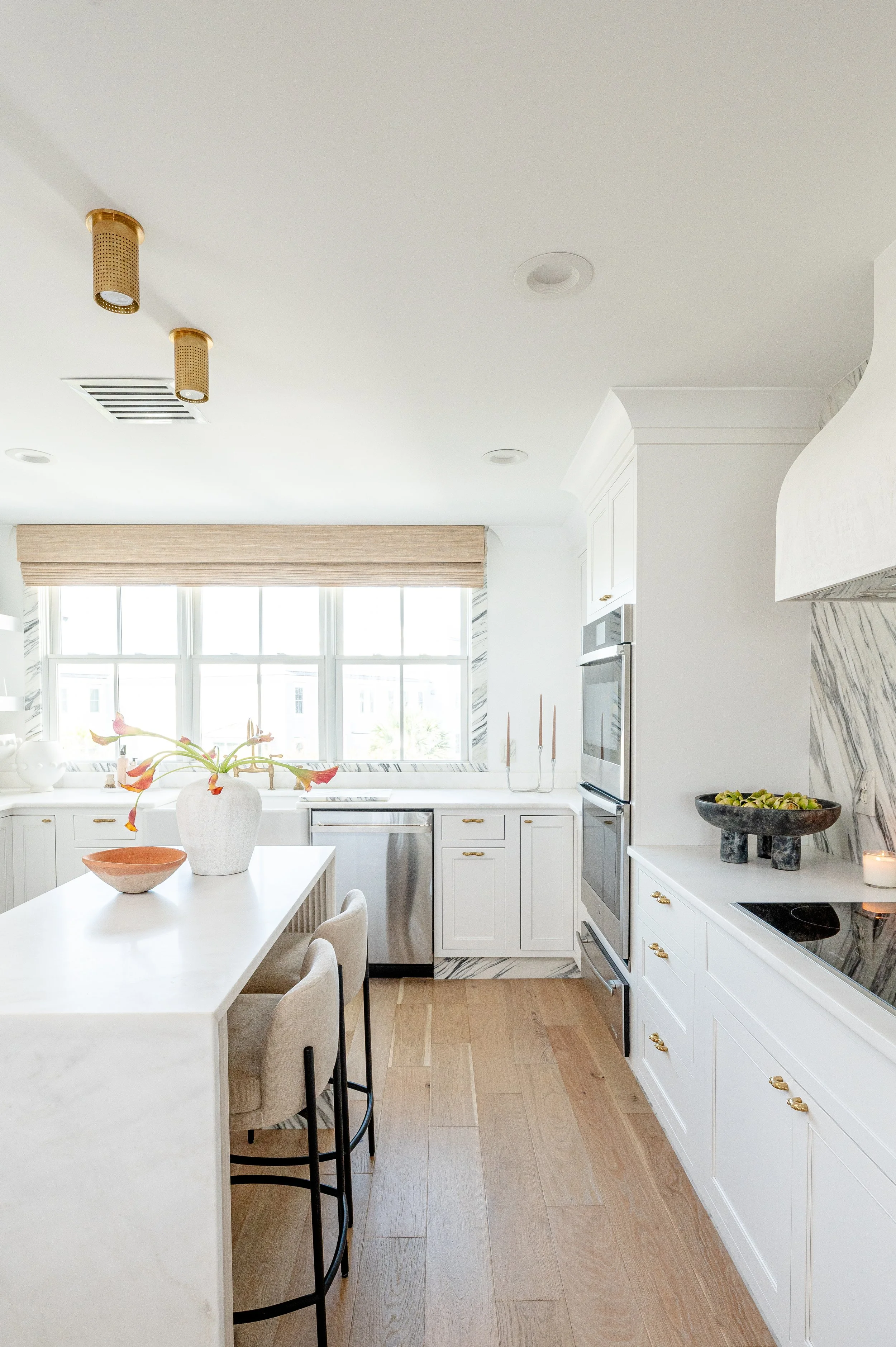 Bright kitchen with white cabinets, marble backsplash, large window, wooden floor, and modern appliances.