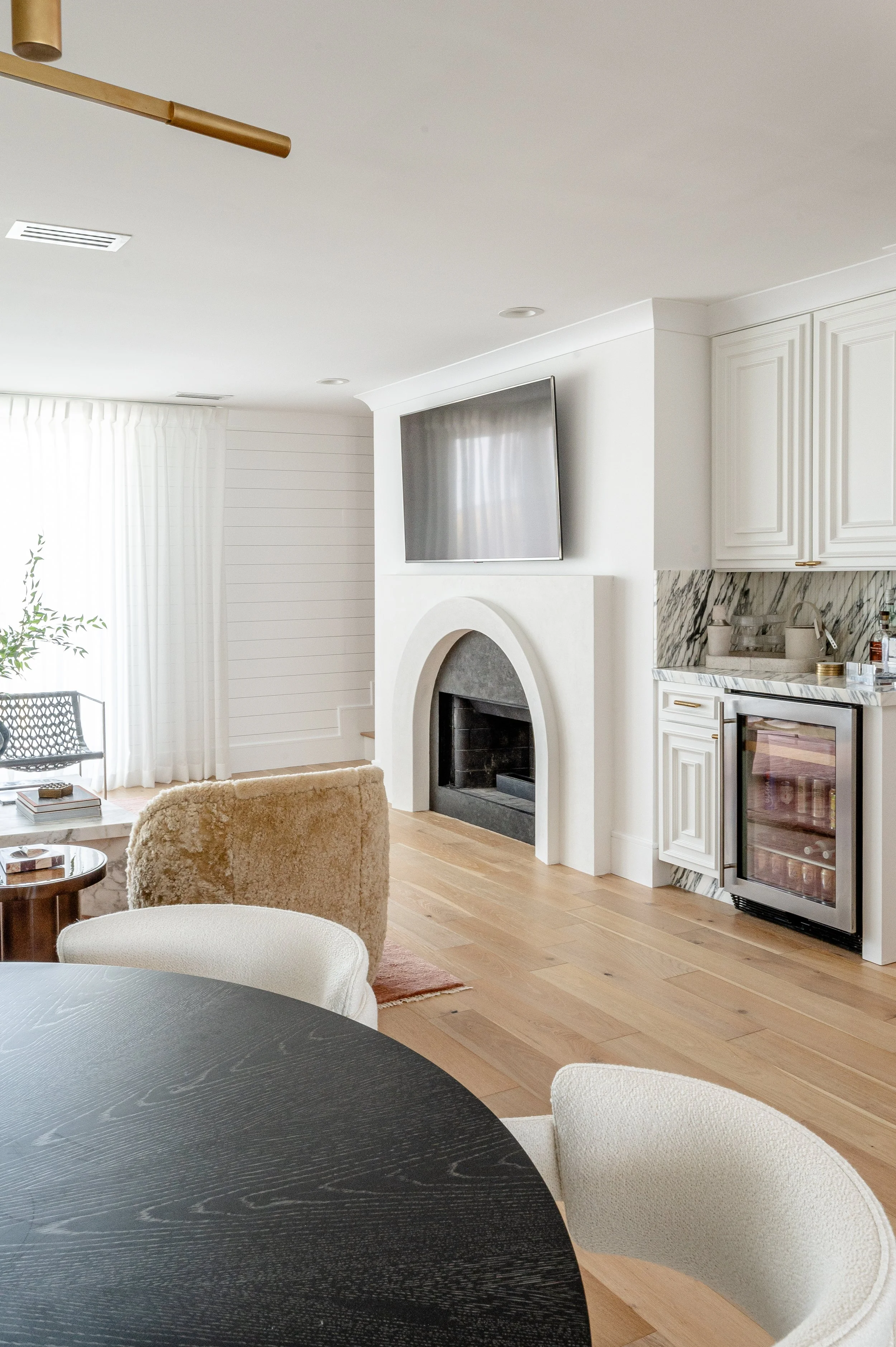 Modern living room with white walls, a fireplace, a mounted flat-screen TV, and a small bar area with a mini fridge.