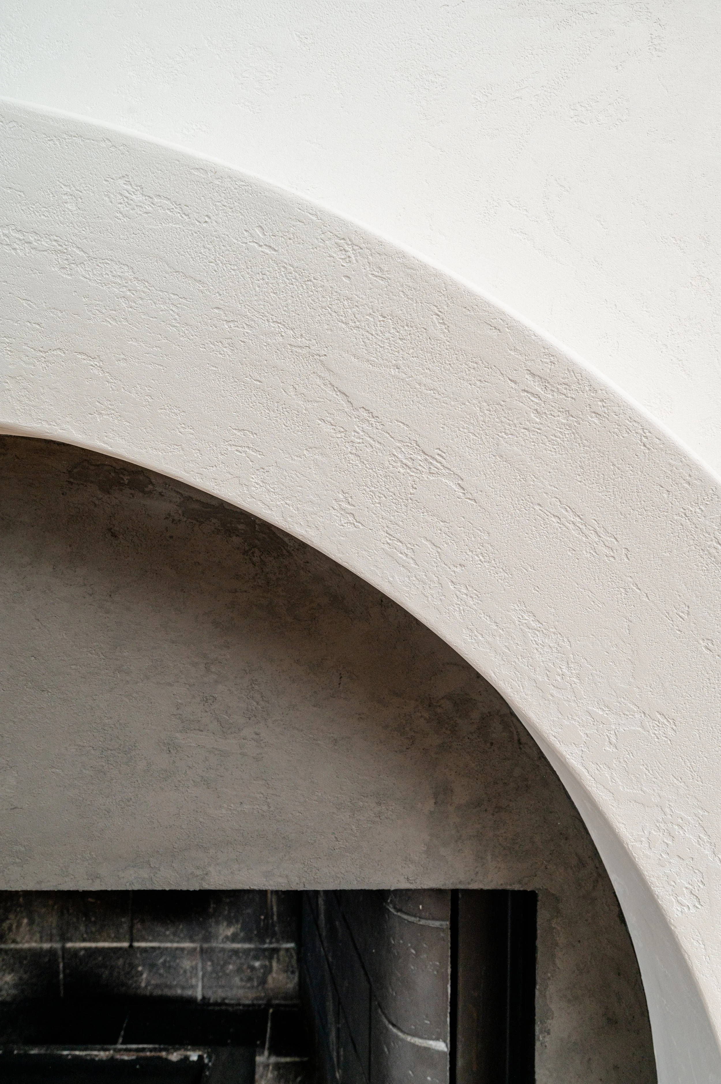 Close-up of a textured, white stucco wall above a dark, tiled fireplace opening.