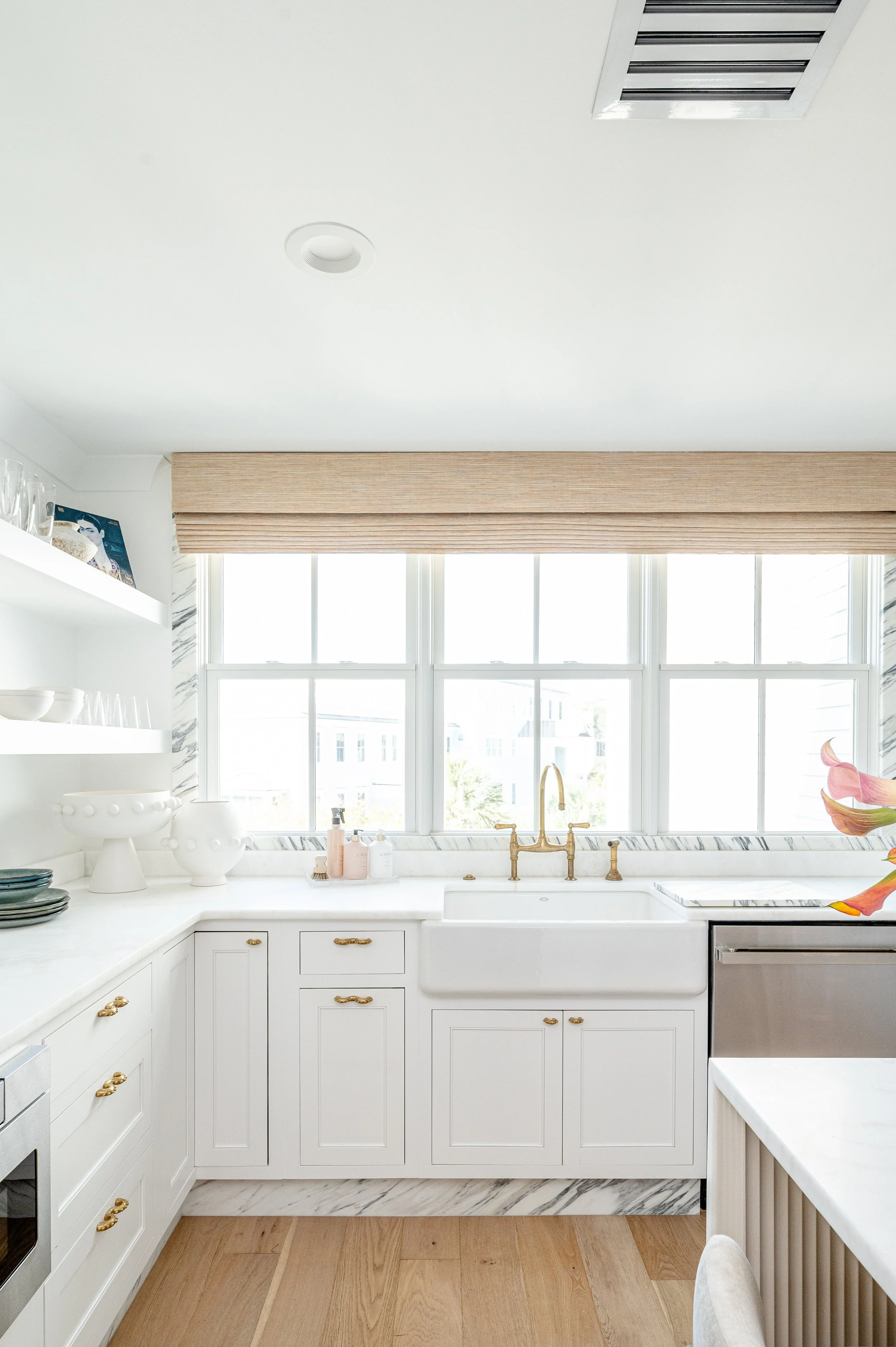 Bright modern kitchen with white cabinets, marble accents, and a large window with a wooden valance.