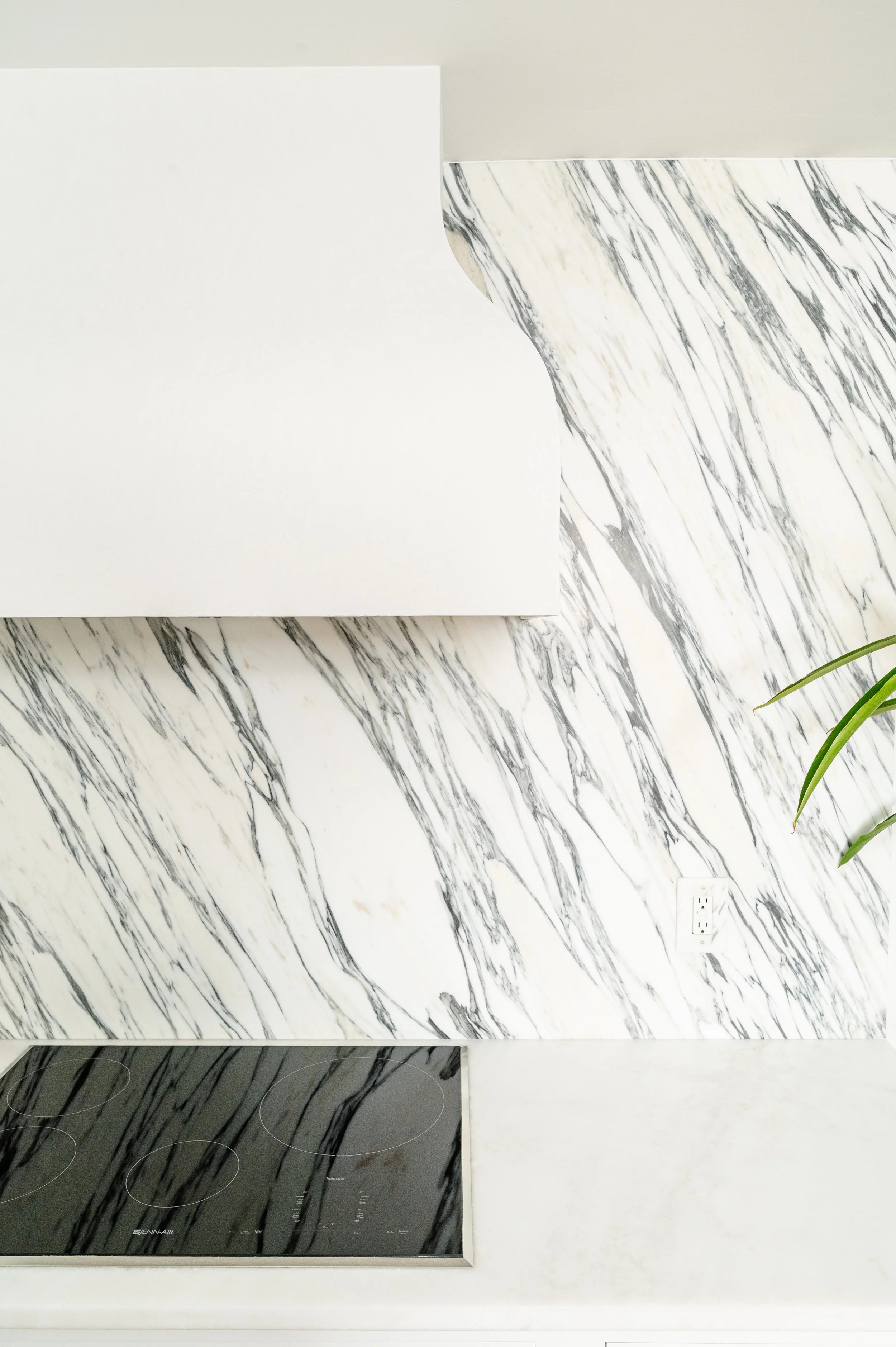 Kitchen countertop with black cooktop, white marble backsplash, and part of a white cabinet.
