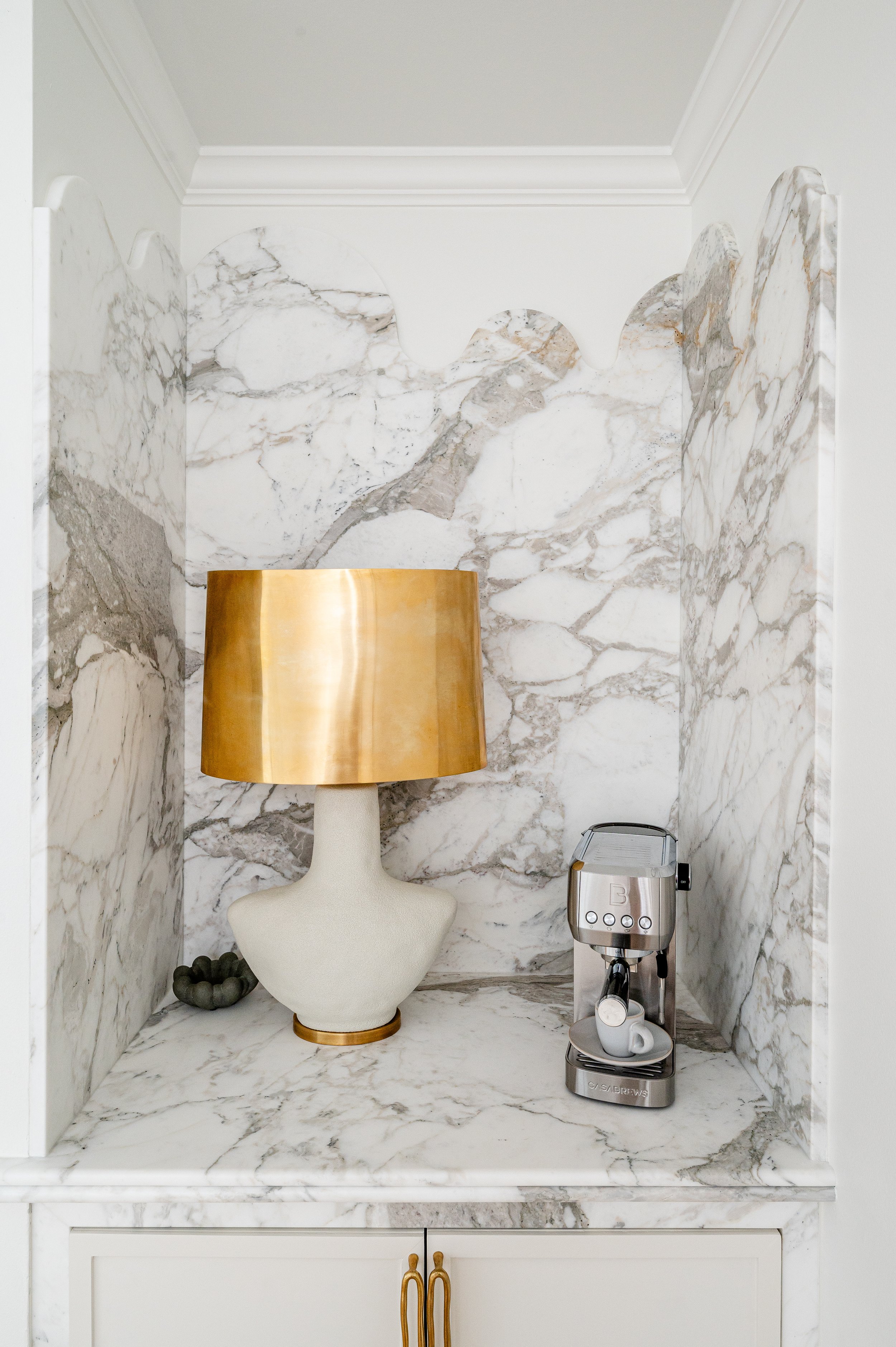 A decorative marble alcove with a ceramic lamp, a stainless steel coffee machine, and a ceramic cup.