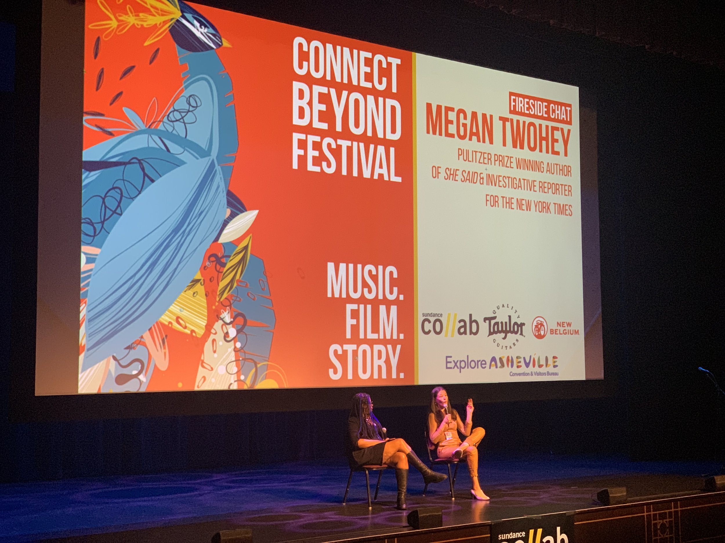 Two women sitting on chairs on a stage in front of a large colorful screen at the Connect Beyond Festival, promoting a fireside chat with Megan Twohey about her work as a Pulitzer Prize-winning author and investigative reporter, with logos of sponsors at the bottom.